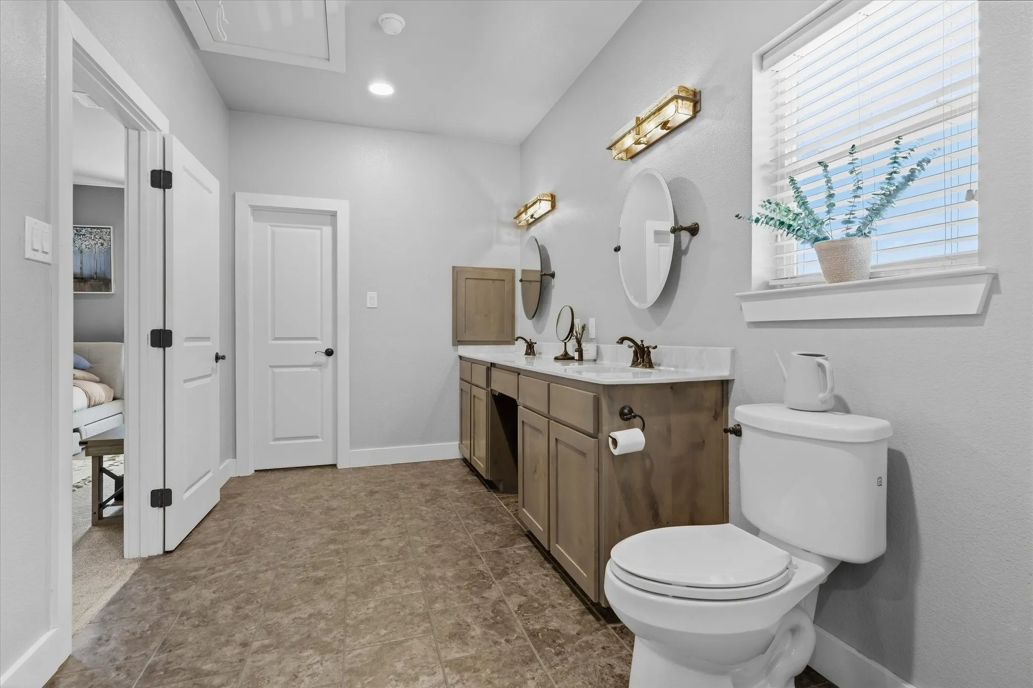 Dual vanity with integrated sinks, wood-finish cabinetry, and wall-mounted lighting