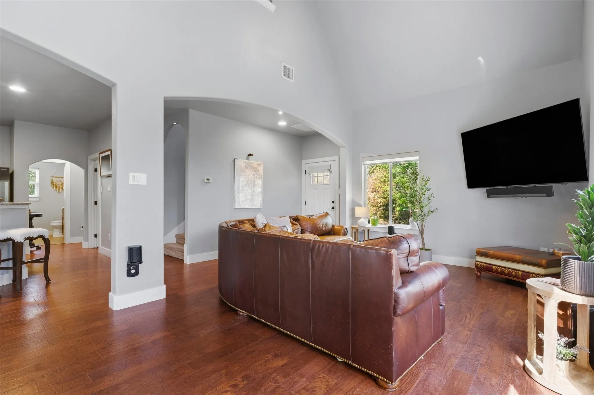 Vaulted ceiling with recessed lighting, wood-finish flooring, white trim, arched doorways, and a front entry door with glass panels