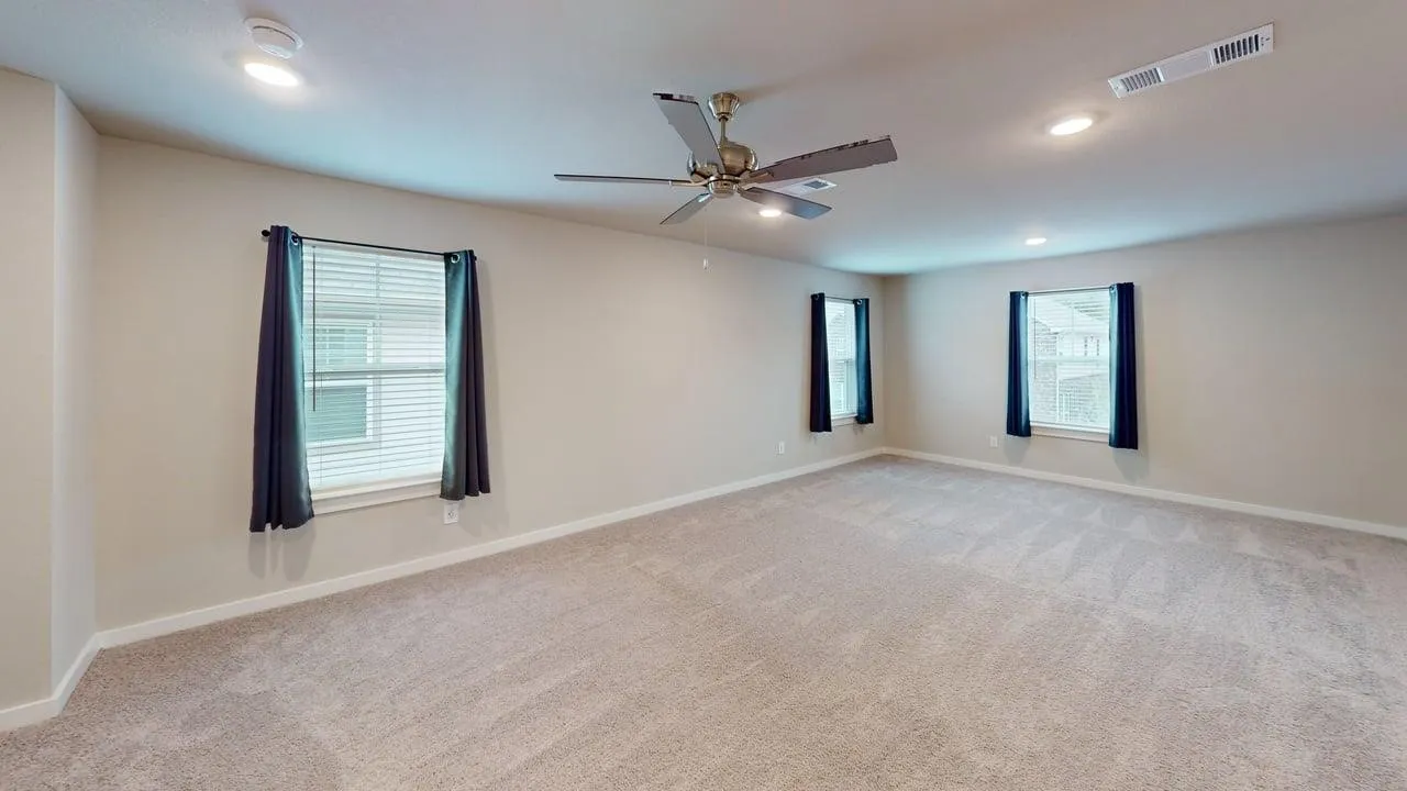Expansive carpeted room featuring recessed lighting, a ceiling fan with light, and multiple windows