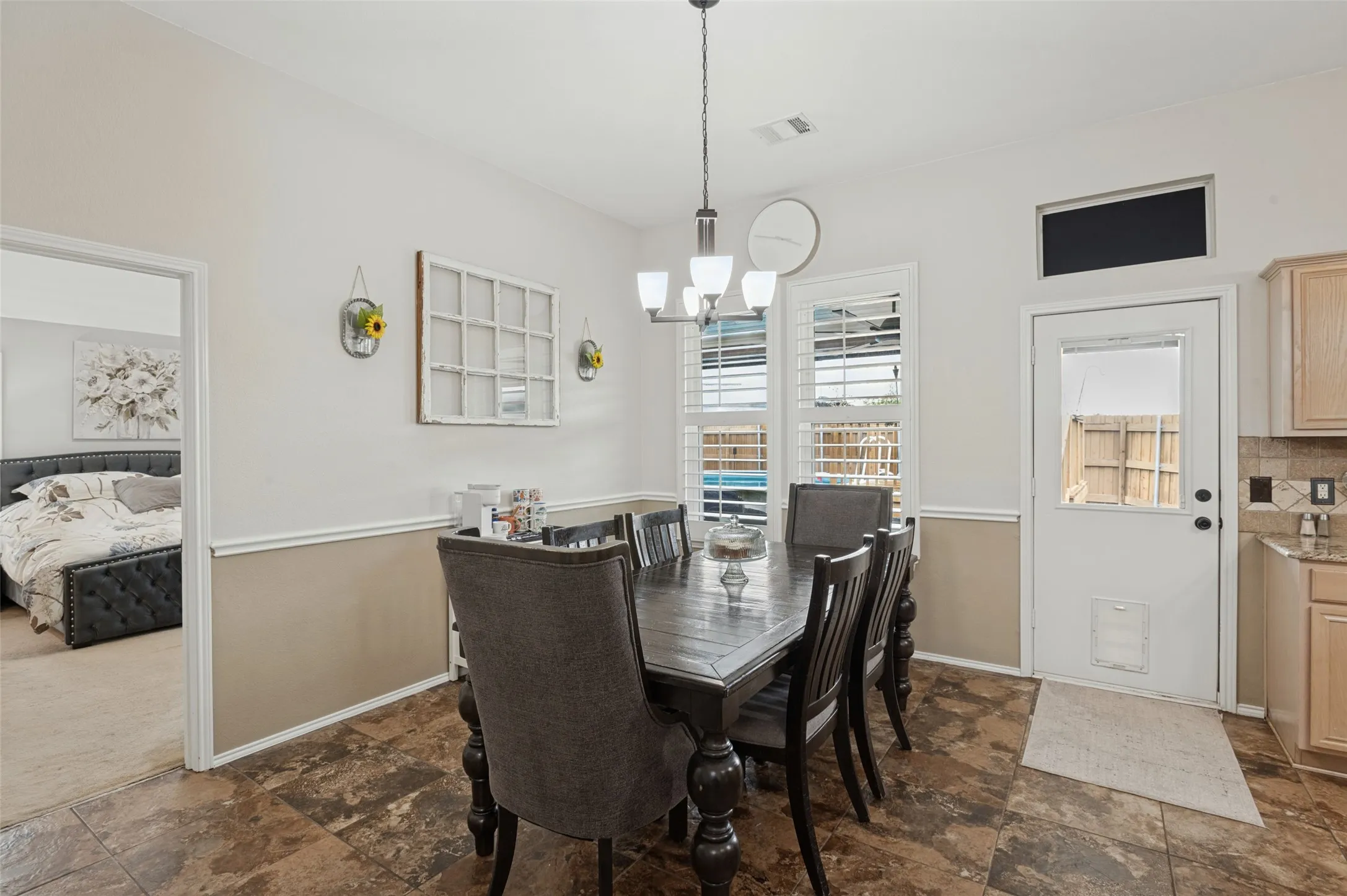 Dining area featuring durable tile flooring, a contemporary chandelier, white window shutters, and a white exterior door with glass paneling