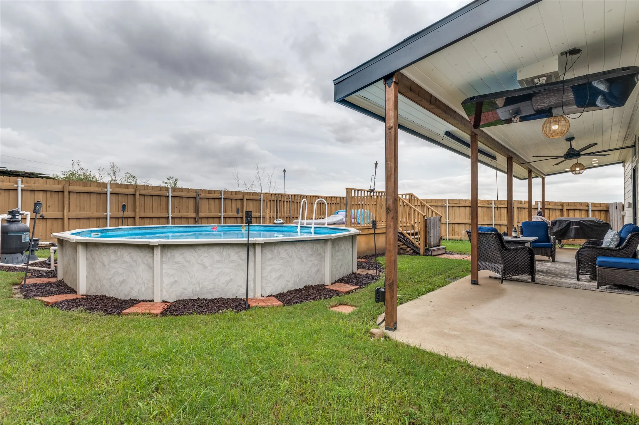Expansive concrete patio with wood-post pergola, dual ceiling fans, and an above-ground pool