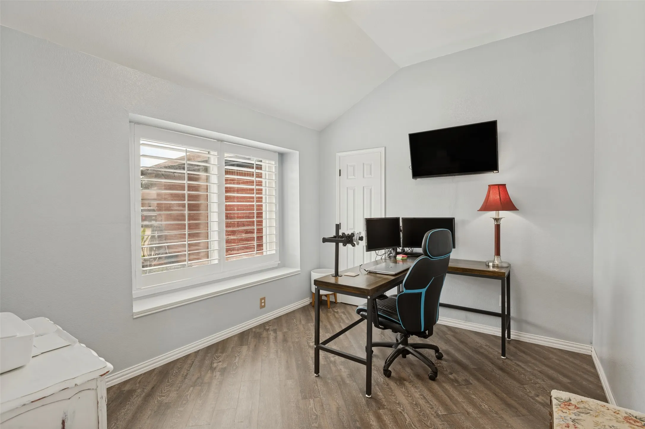 Vaulted ceiling, wood-finish flooring, white window shutters, light gray walls, and a white paneled door