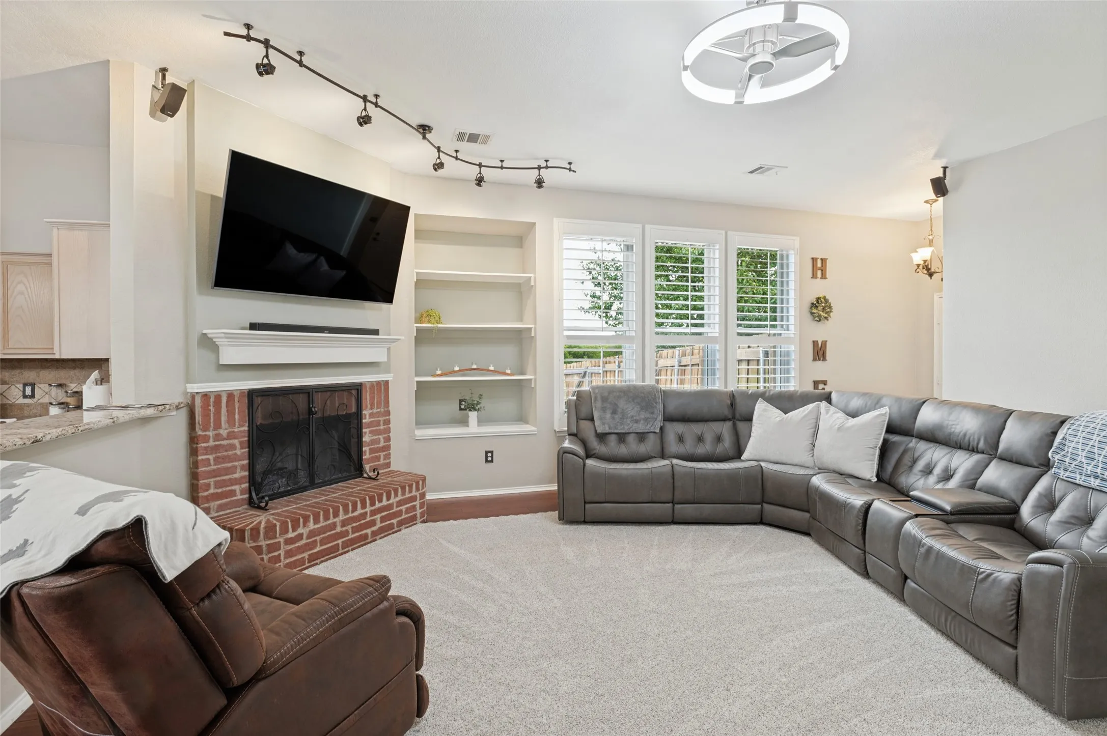 Recessed fireplace with a brick hearth, built-in shelving, track lighting, and multiple windows with plantation shutters