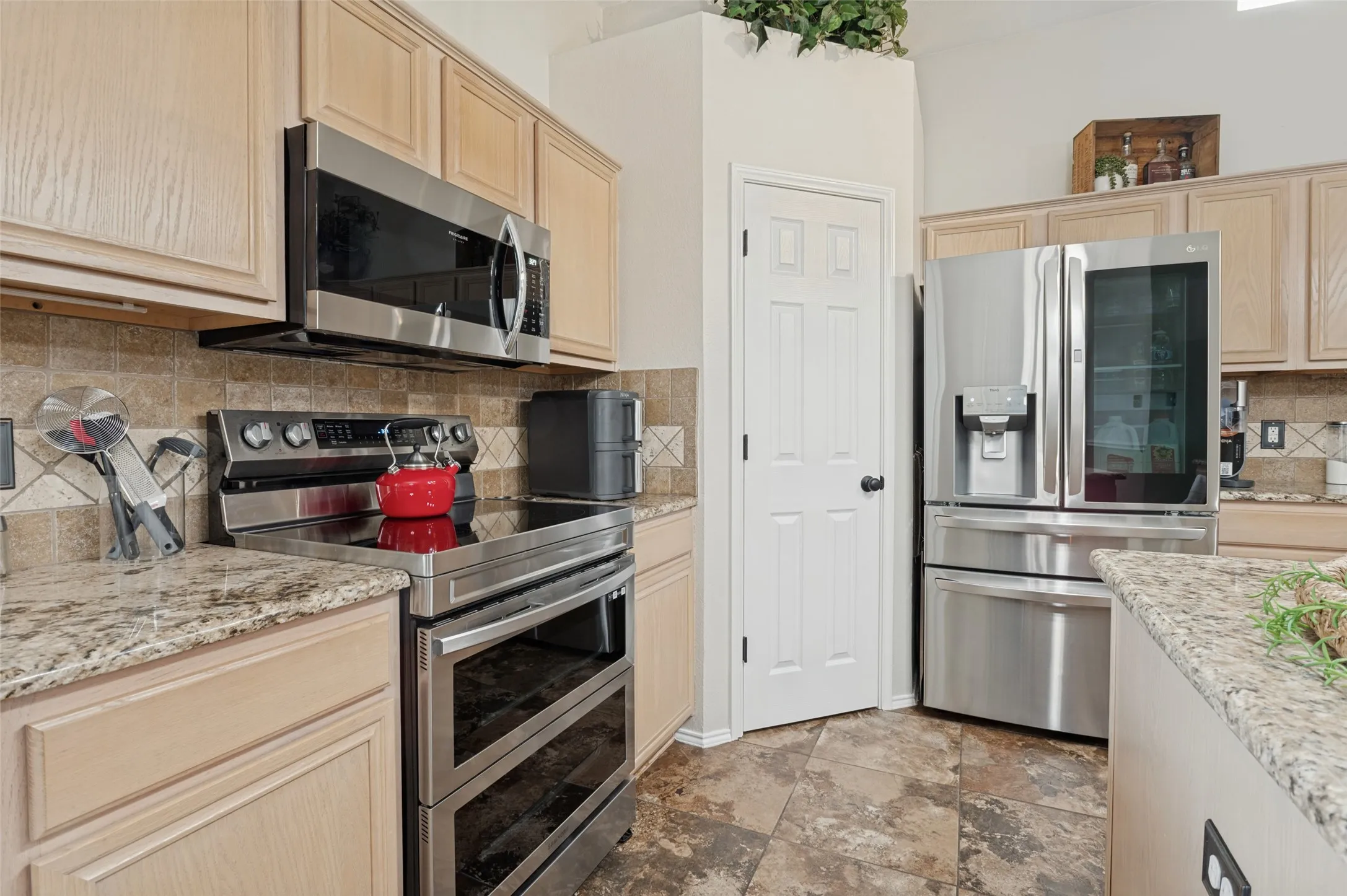 Kitchen featuring light wood cabinetry, stone-finish countertops, stainless steel appliances, and a tiled backsplash