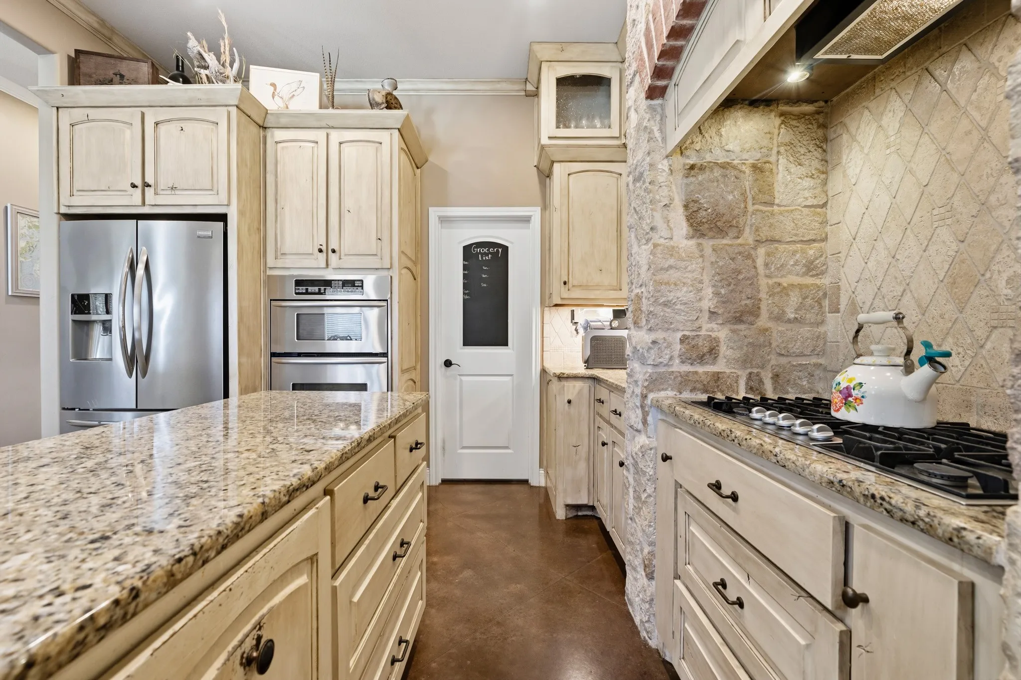 Granite countertops, stone accent wall, tile backsplash, built-in stainless steel double oven, and a built-in gas cooktop