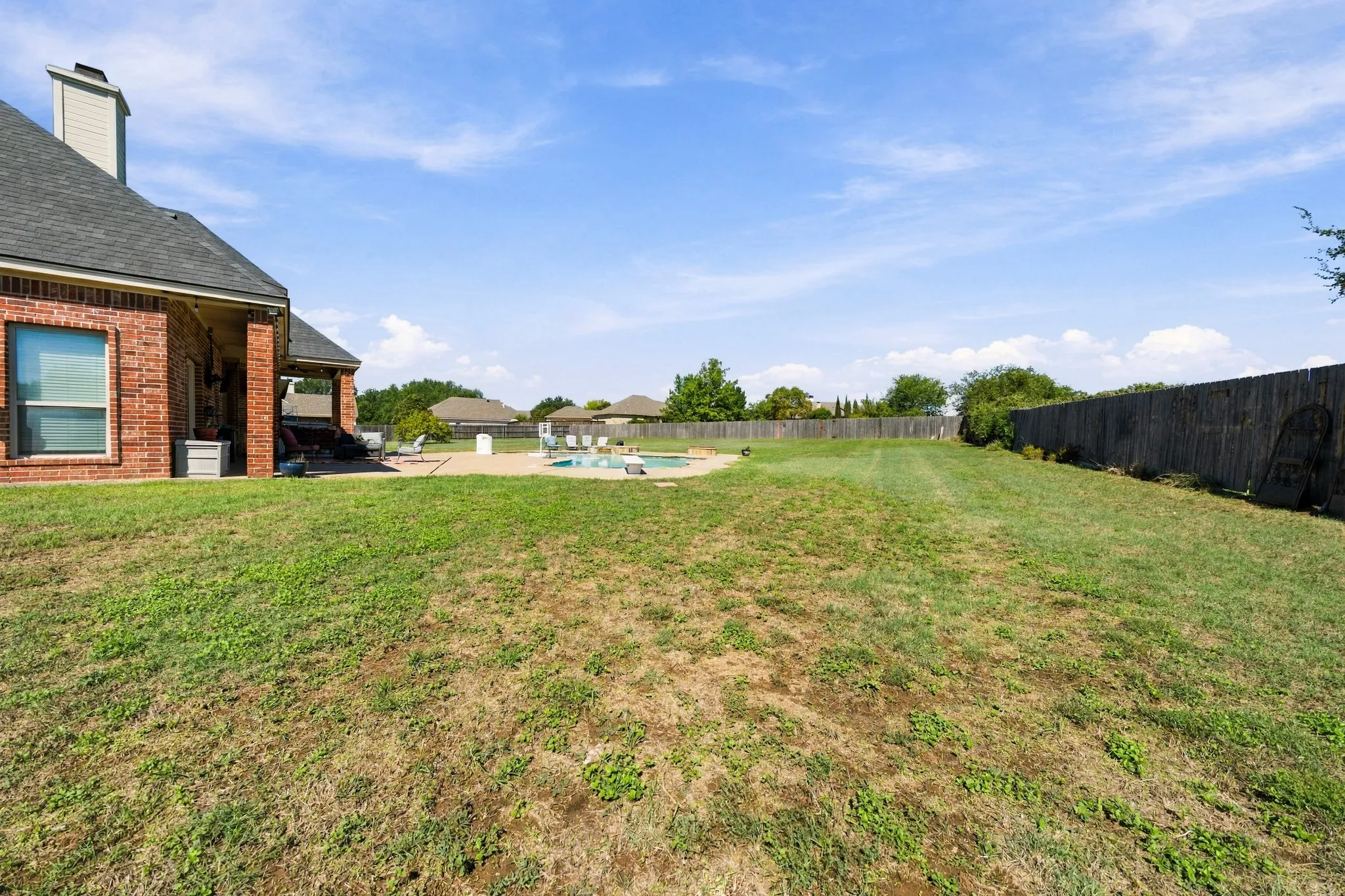Brick exterior with a covered patio, adjacent to a perimeter wooden fence