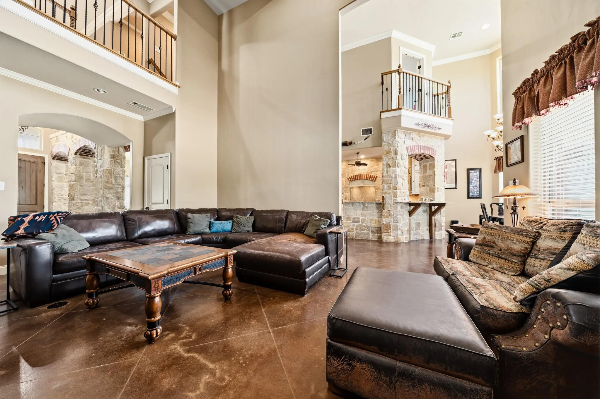 Soaring ceilings, stone-clad architectural elements, and an upper-level balcony with metal balusters
