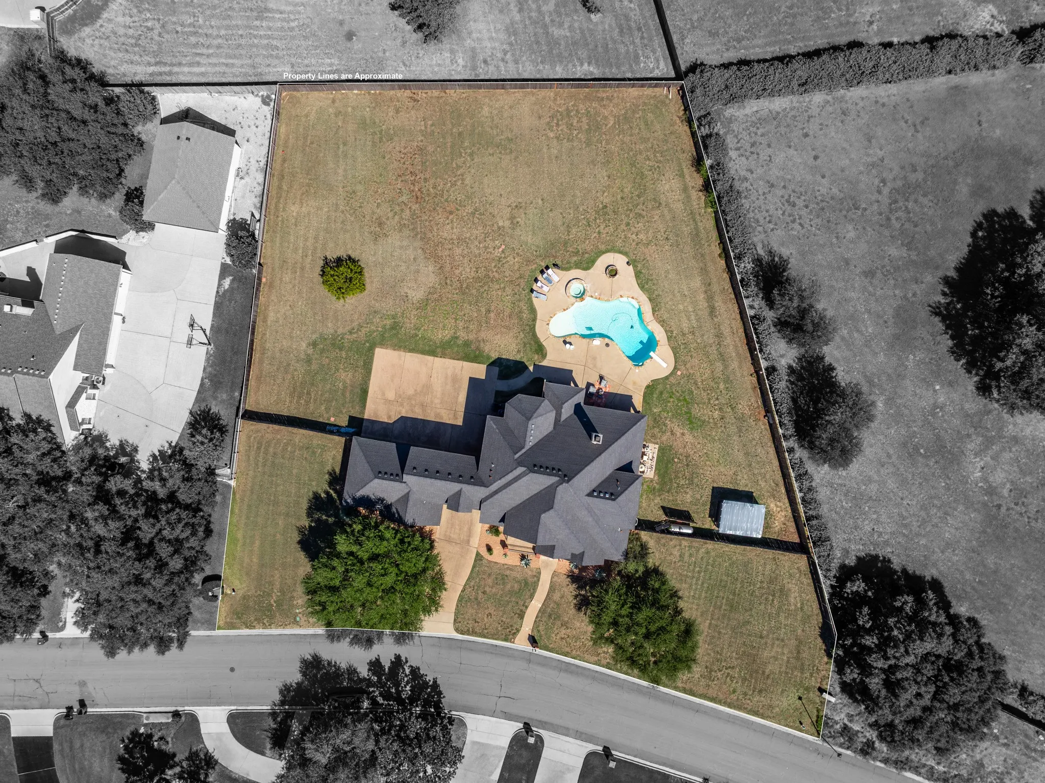 Spacious property featuring a multi-gabled roofline, an irregular-shaped pool with integrated spa, an expansive paved patio, and a dedicated storage shed