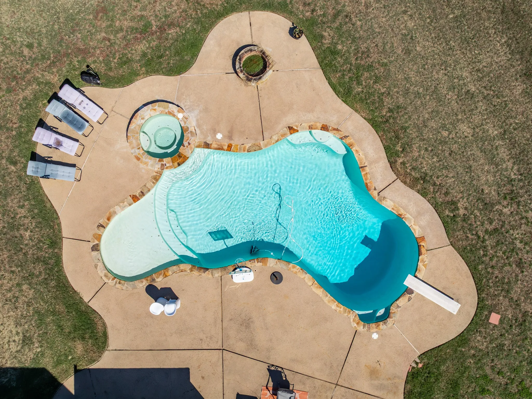 Freeform swimming pool with integrated spa, diving board, and adjacent fire pit, all surrounded by a concrete deck