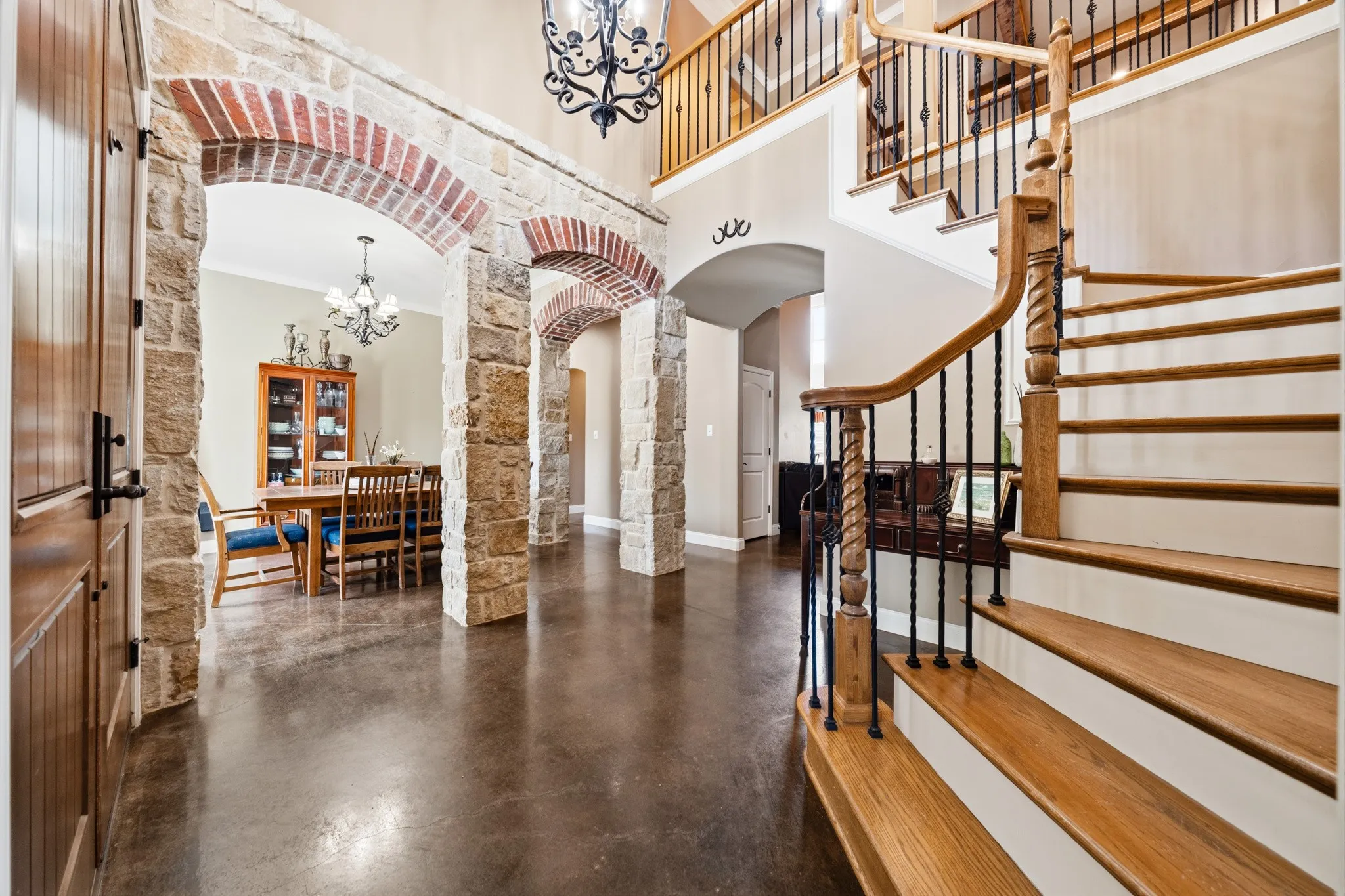 Stone archways with brick accents, wood-finish flooring, a two-story ceiling, a wrought iron chandelier, and a wood spiral staircase