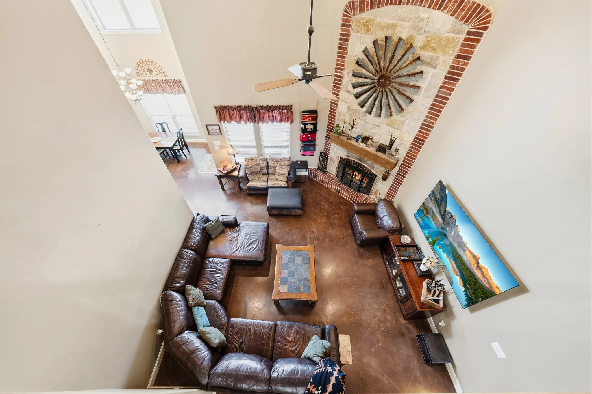 Two-story living area featuring a stone and brick fireplace, ceiling fan, and wood-finish flooring