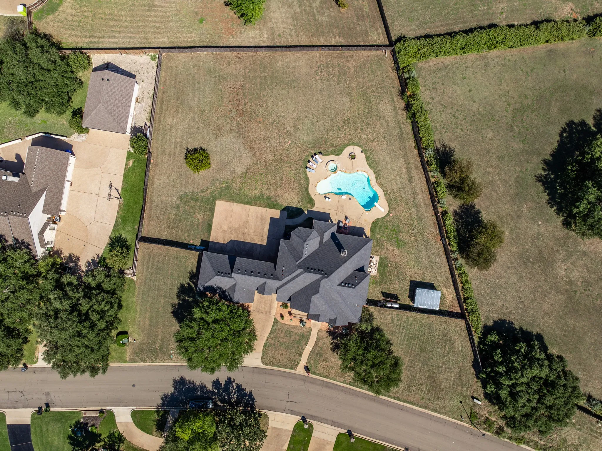 Expansive property featuring a multi-gabled roofline, a freeform swimming pool with integrated spa, a paved drive, and mature trees