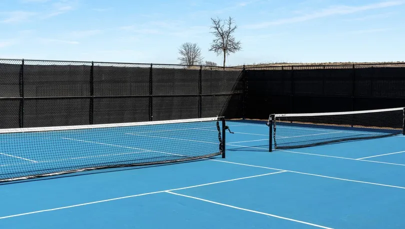 Dedicated tennis court featuring a blue playing surface with white line markings, two nets with black posts, and black perimeter fencing with privacy screening