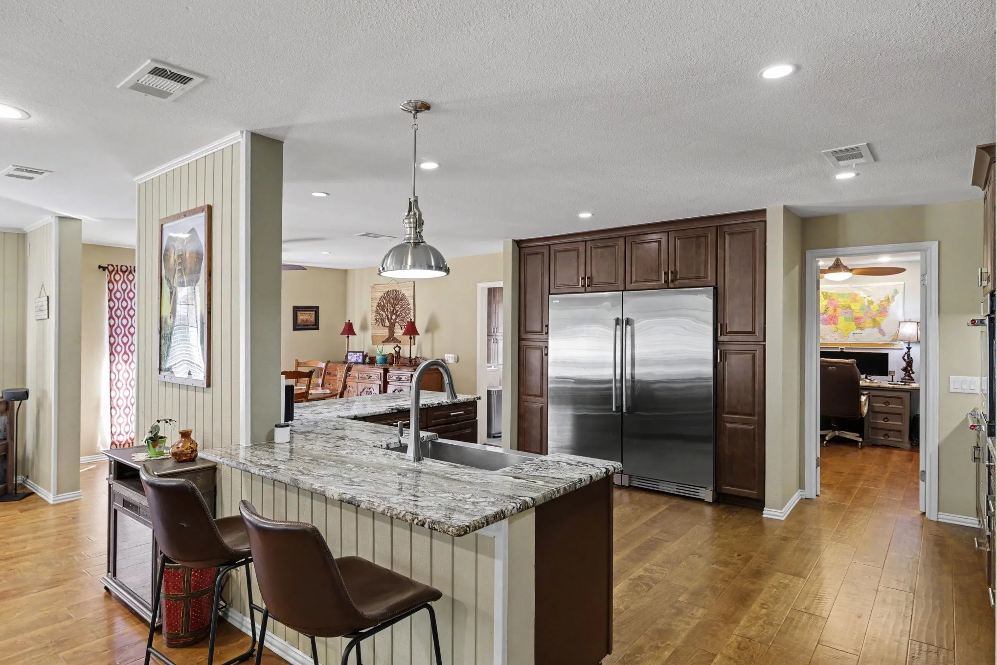 Kitchen featuring wood-finish flooring, a granite-top island with beadboard detailing, dark wood cabinetry, and stainless steel appliances