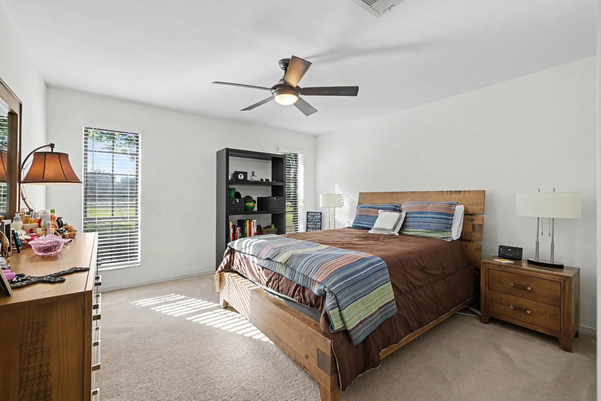 Carpeted room with multiple windows providing natural light, a ceiling fan with integrated lighting, and white wall finishes