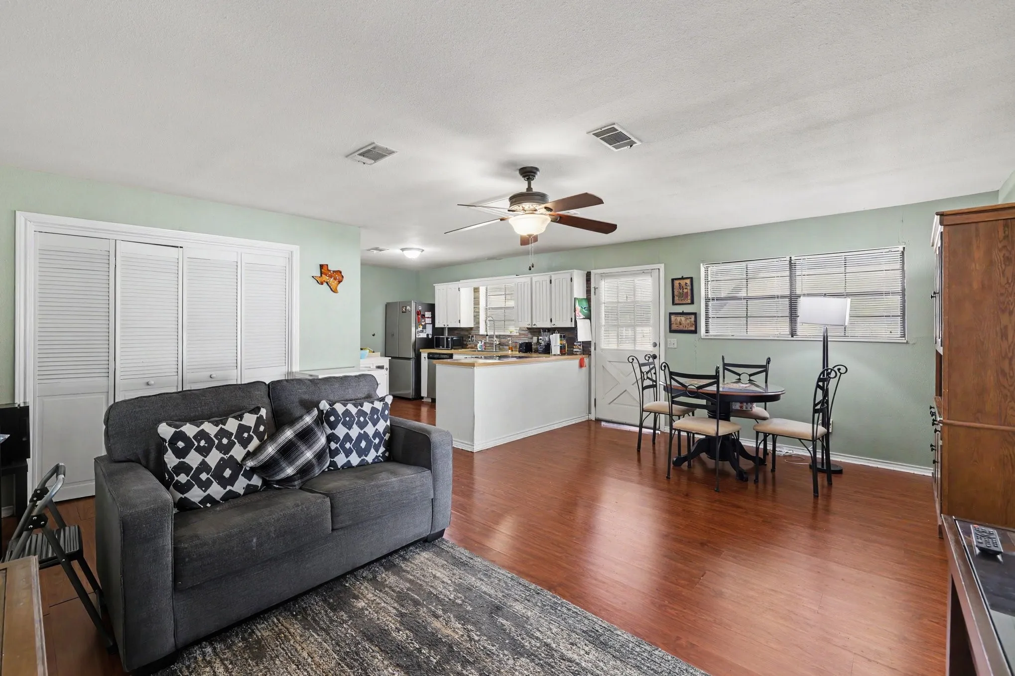 Hardwood-finish flooring, white louvered bifold doors, ceiling fan, white cabinetry, and a kitchen island