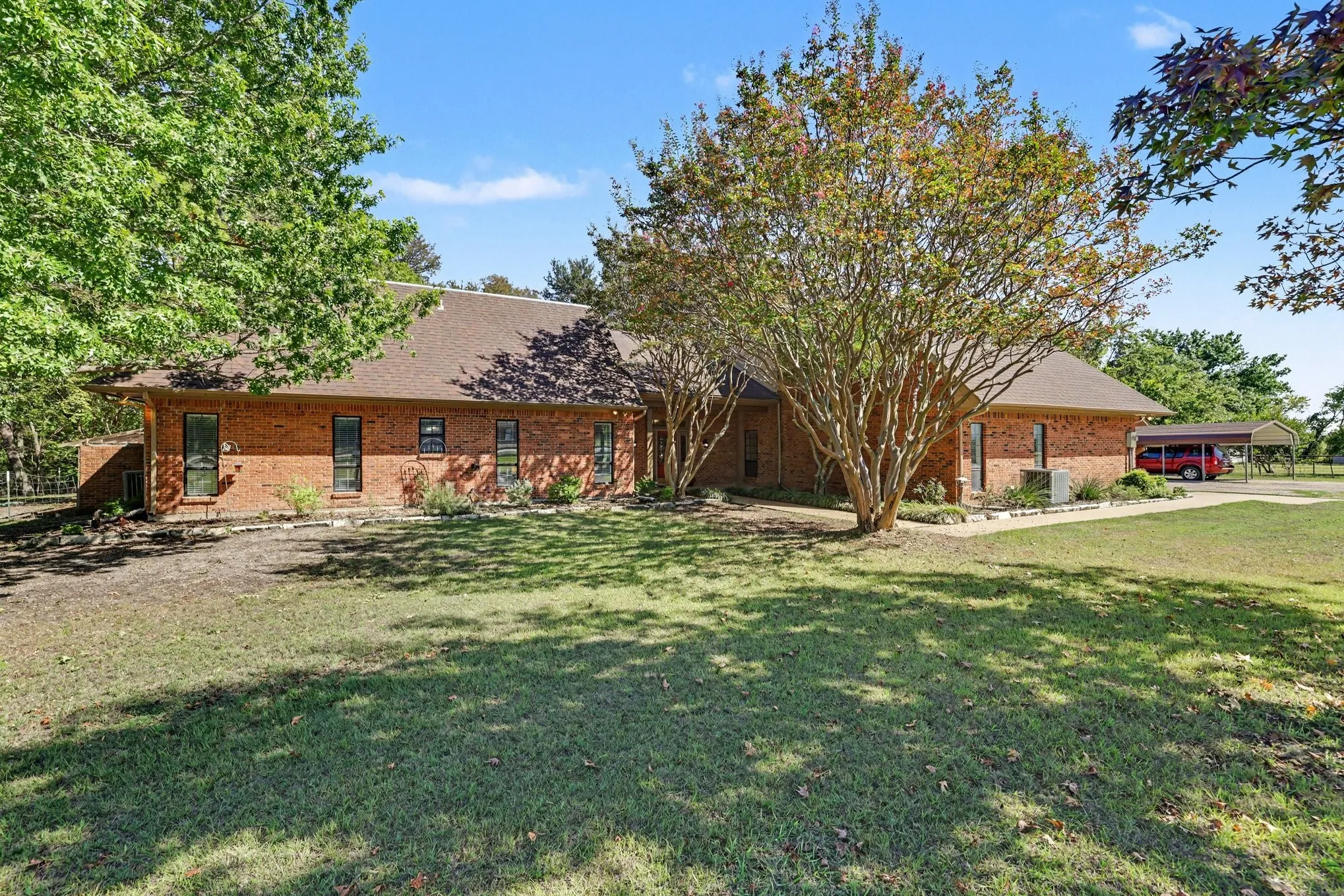 Brick exterior with a shingle roof, mature landscaping, and an attached carport