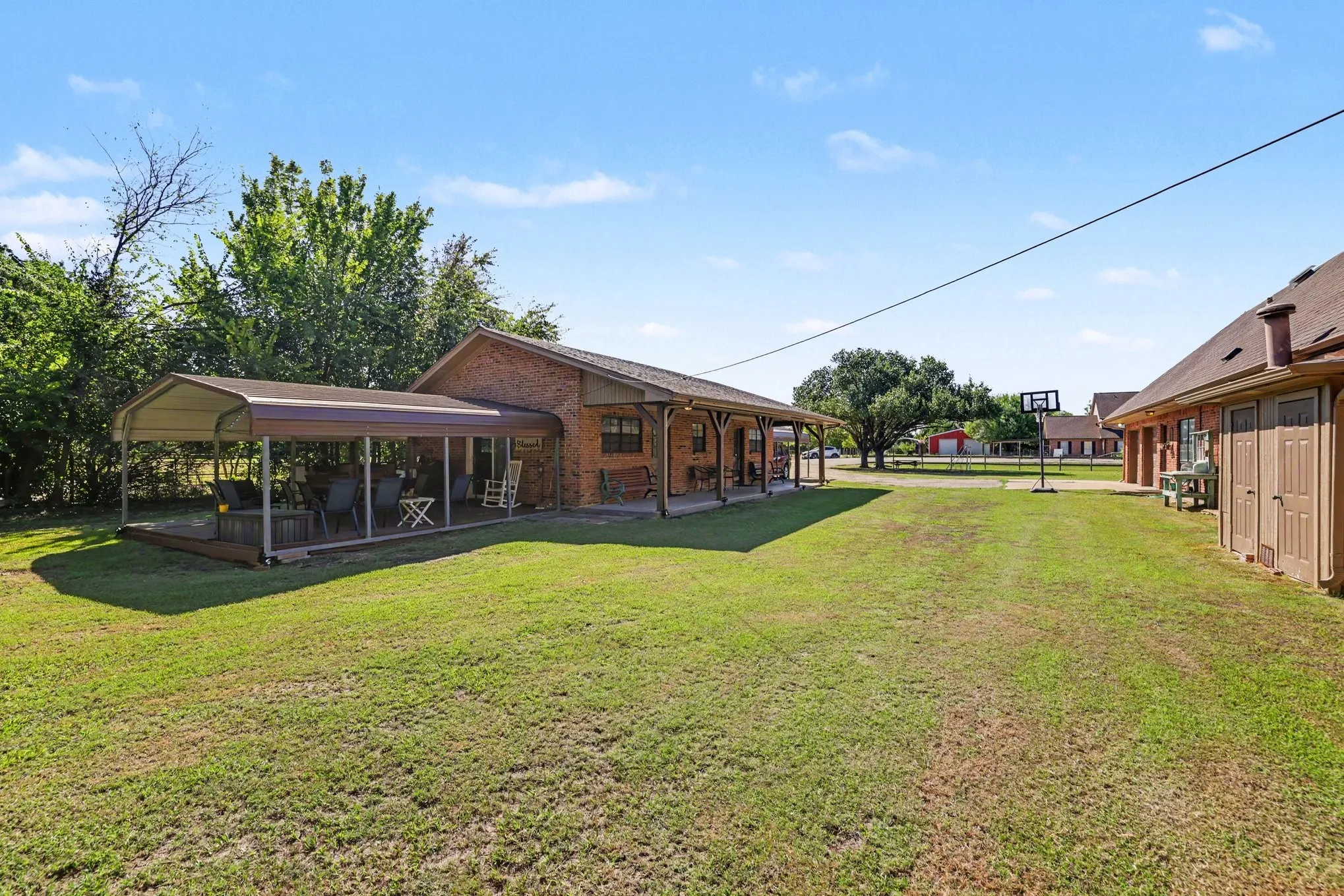 Expansive grassy yard area with a large covered patio featuring a metal frame and roof, brick exterior, and a secondary structure with exterior doors