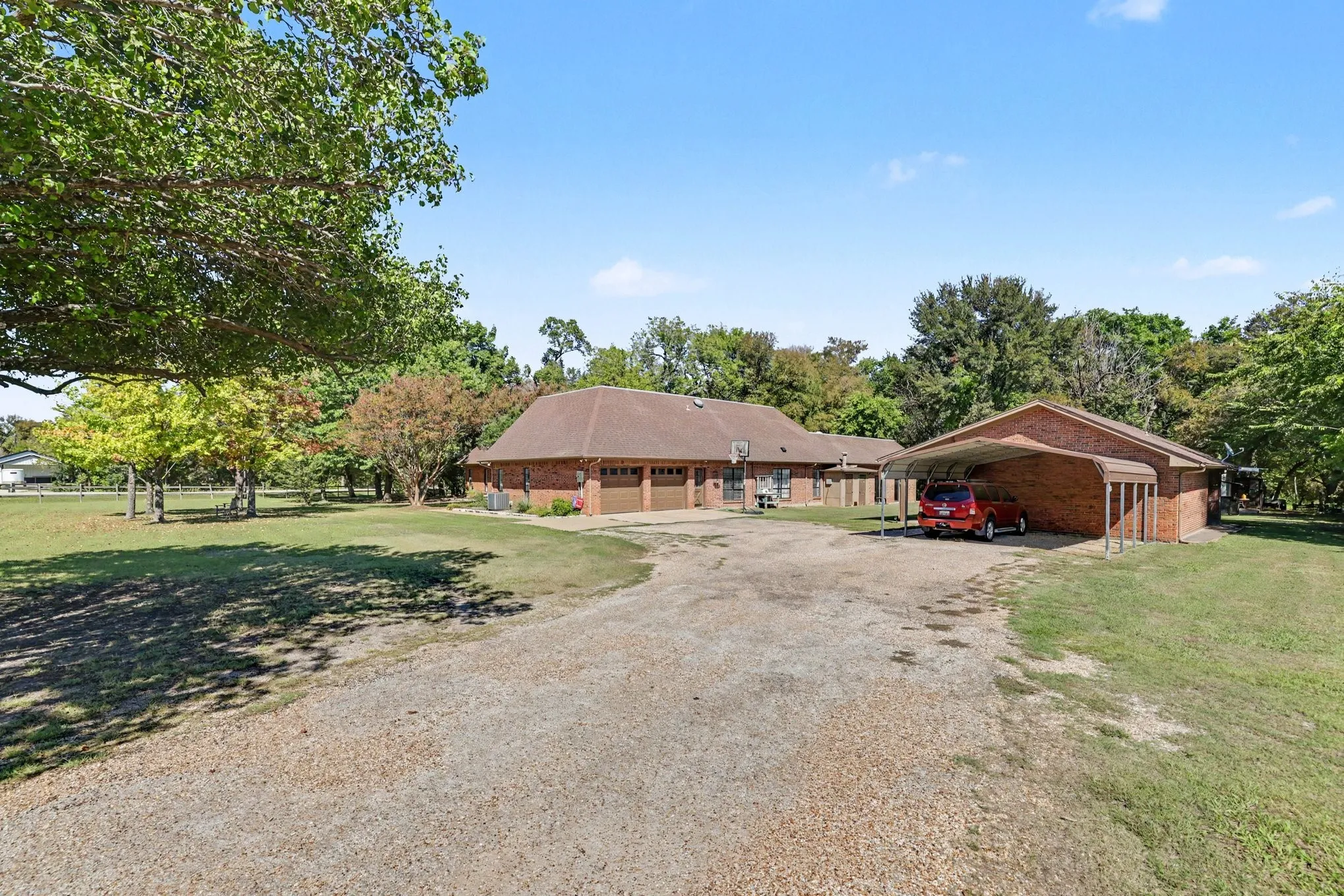 Brick exterior residence featuring a two-car garage, expansive gravel driveway, and a detached carport