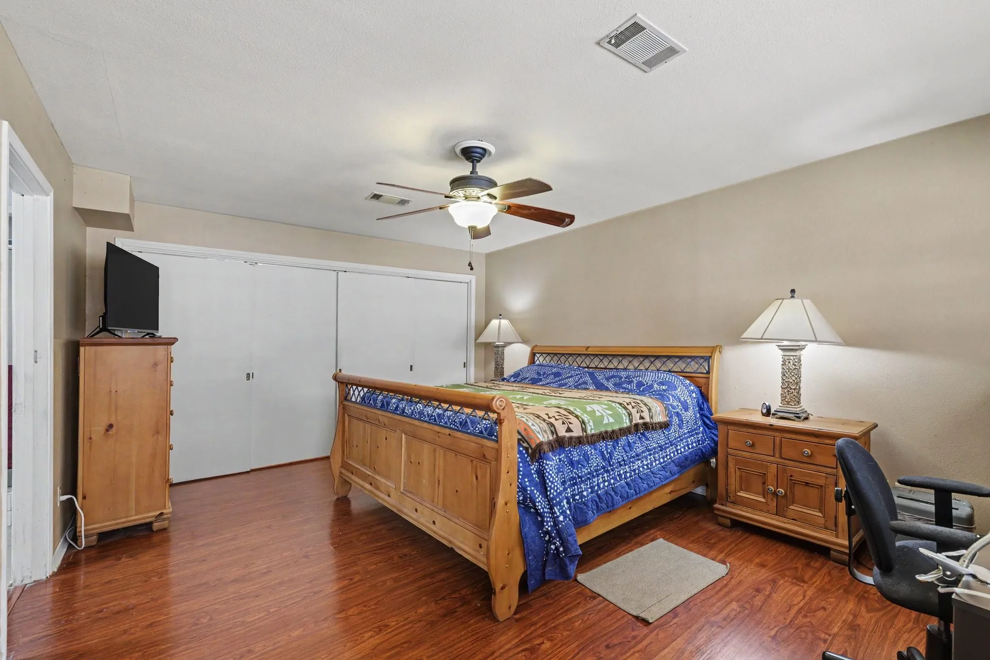 Wood-finish flooring throughout, ceiling fan with integrated lighting, and multiple sliding closet doors