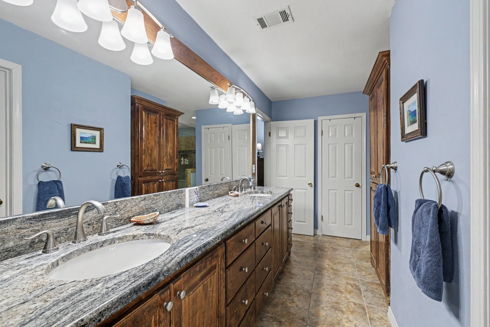 Double vanity with undermount sinks, stone countertop, brushed nickel fixtures, custom wood cabinetry, and a full-width mirror
