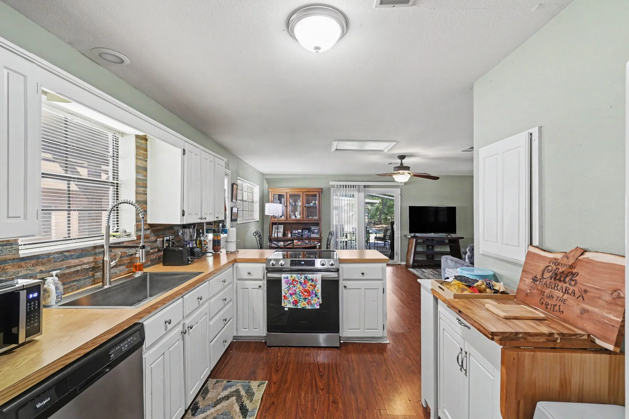 White cabinetry with modern hardware, wood-finish countertops, stainless steel sink, and stacked stone-finish backsplash