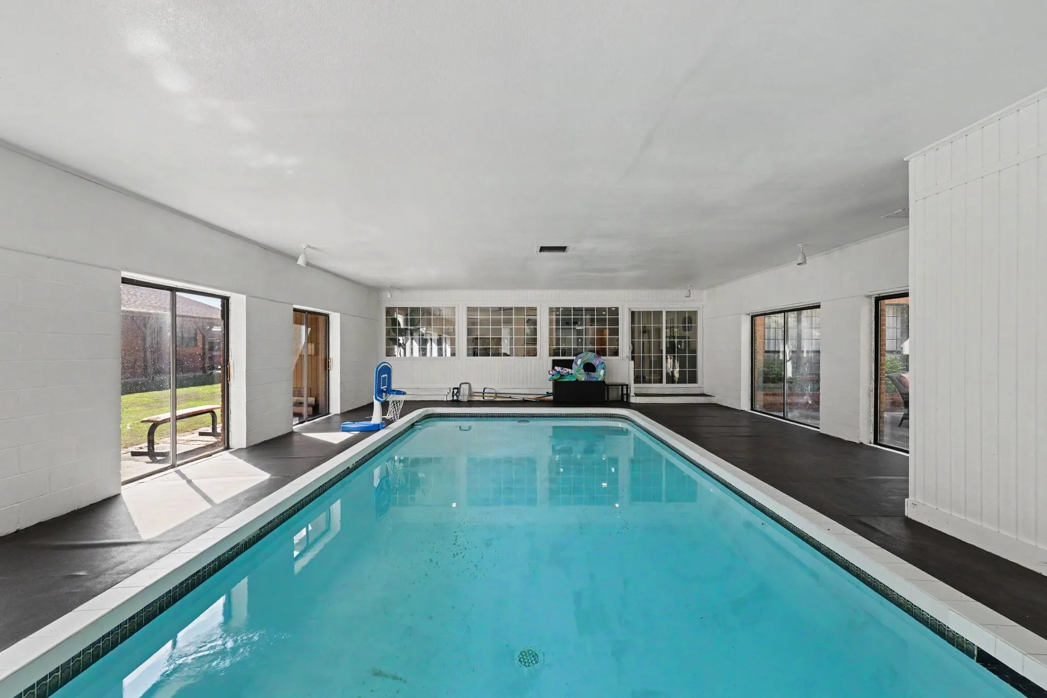 Indoor swimming pool with perimeter tiling, multiple large glass sliding doors, transom windows, and white vertical paneling