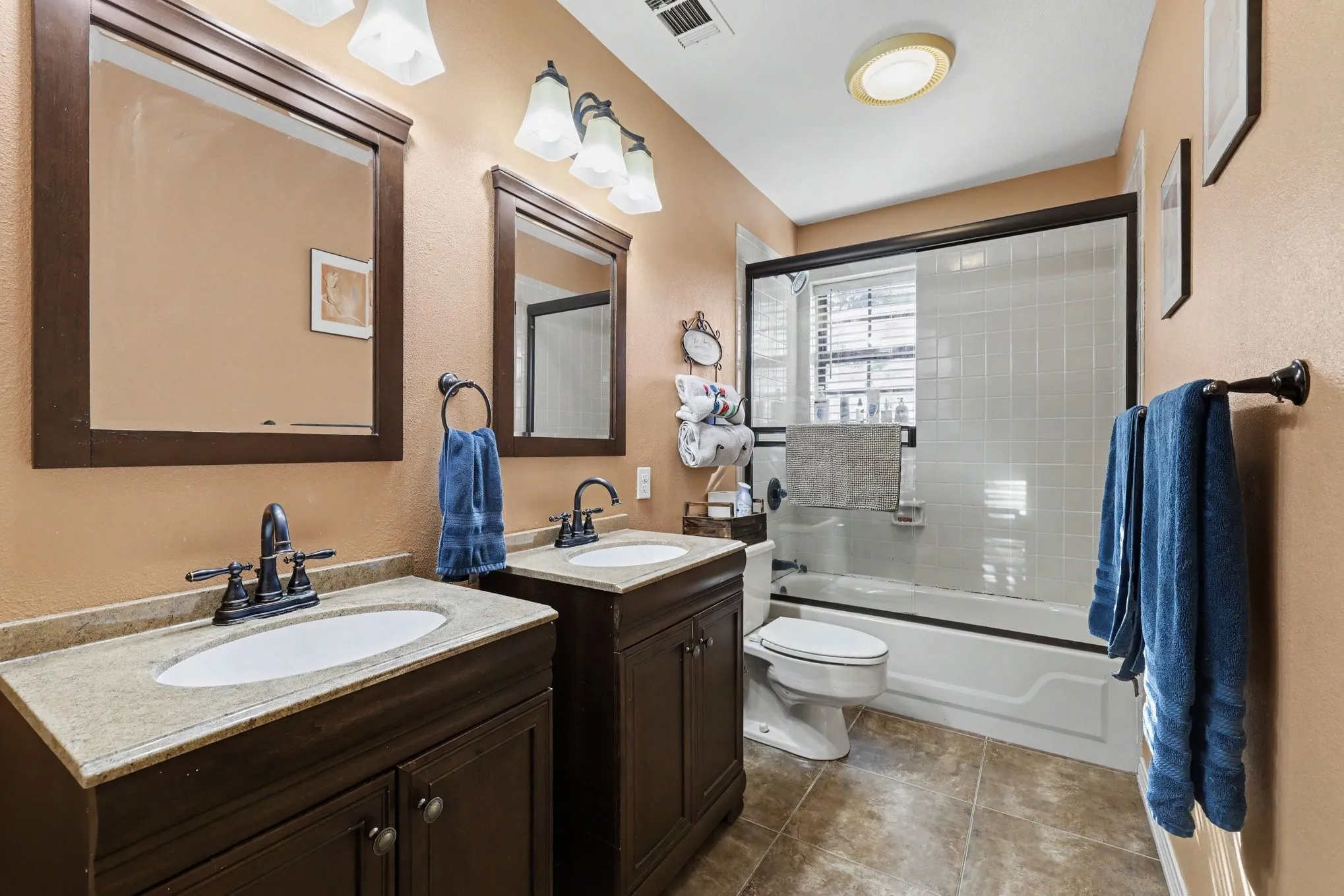 Dual vanity with granite-style countertops and undermount sinks, bronze-finish fixtures, and a shower-tub combination with a sliding glass enclosure