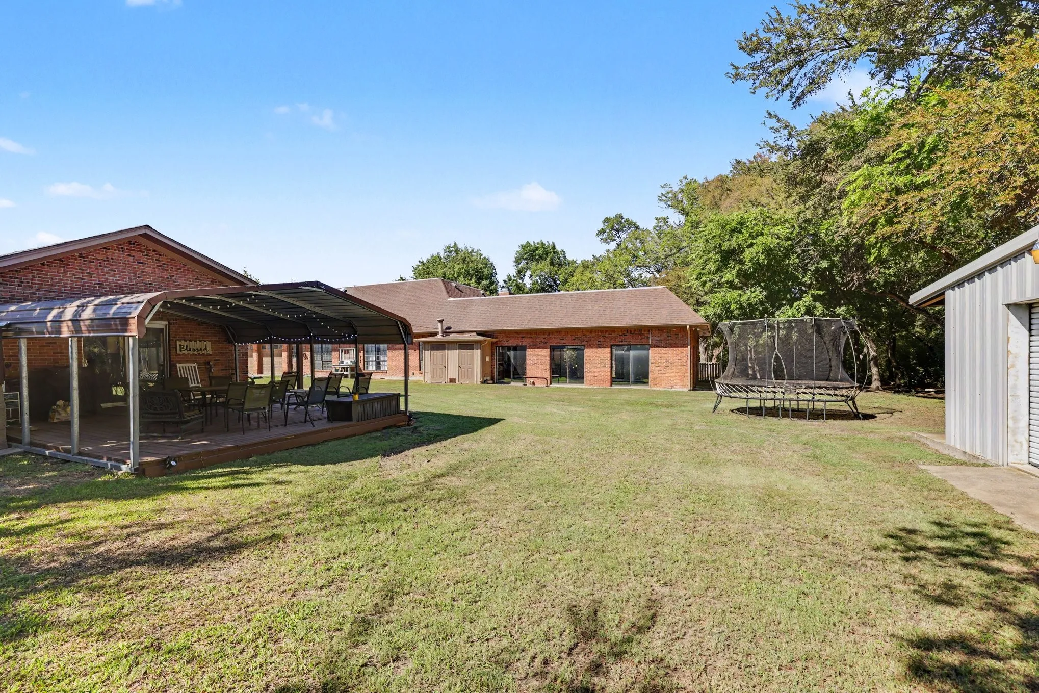 Expansive backyard with a covered patio deck, brick exterior, multiple sliding glass doors, and a detached corrugated metal structure