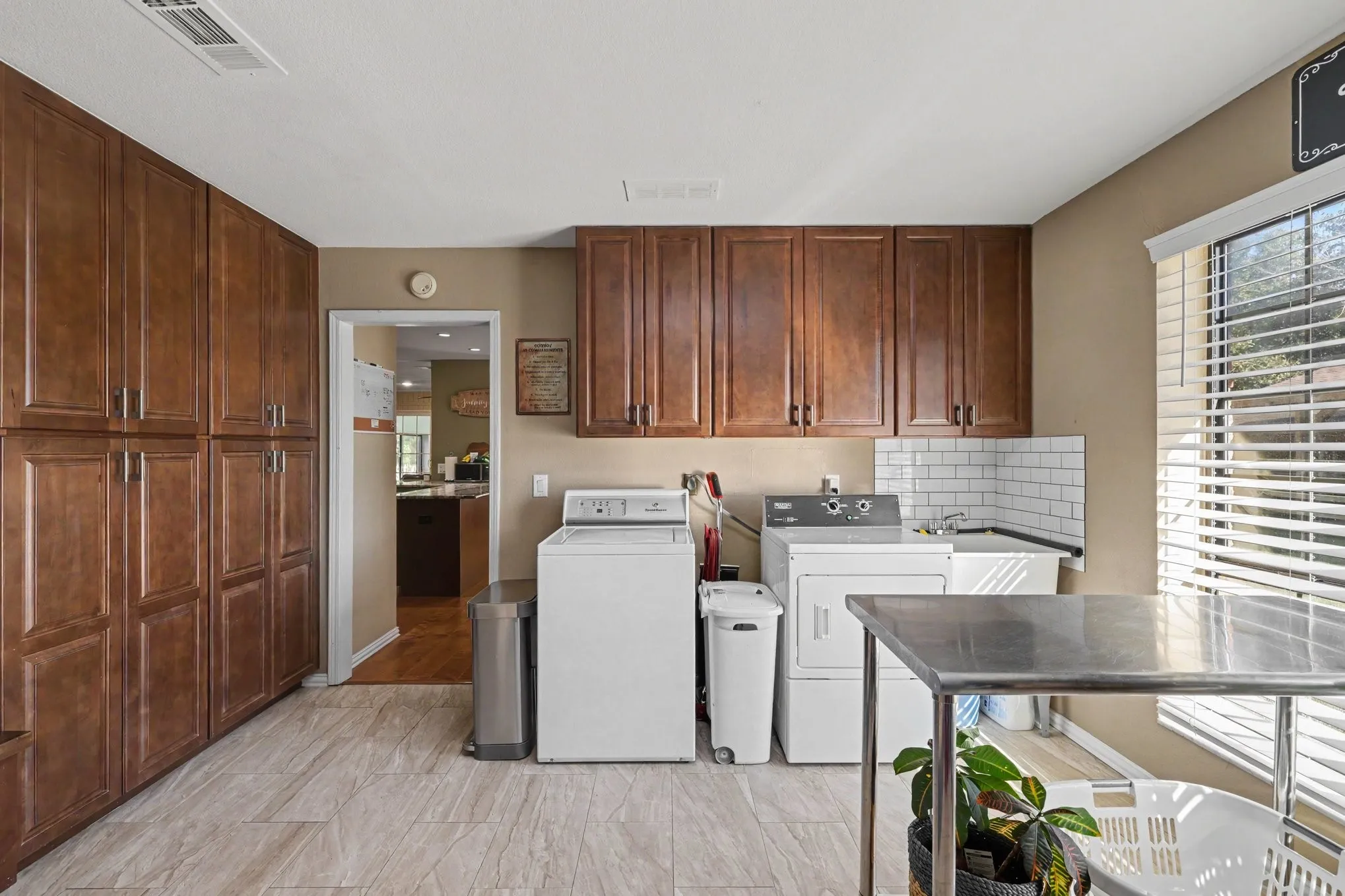 Dedicated utility room featuring extensive built-in cabinetry, ceramic tile flooring, a utility sink with subway tile backsplash, and a window with blinds