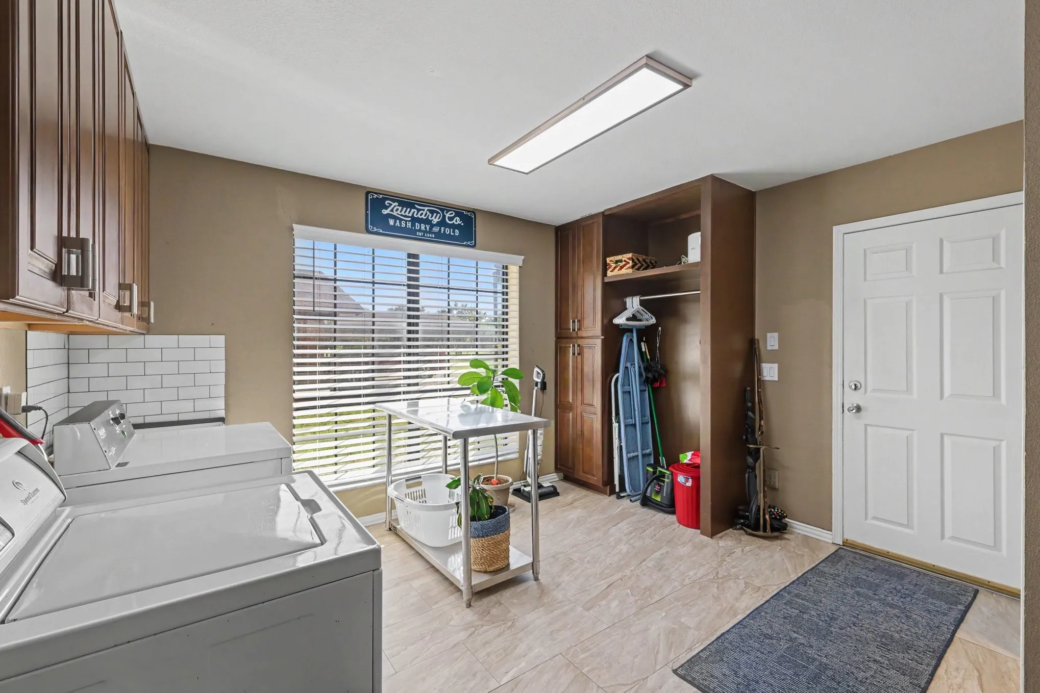 Upper wood-finish cabinetry, subway tile backsplash, tiled flooring, window with blinds, and built-in storage solutions
