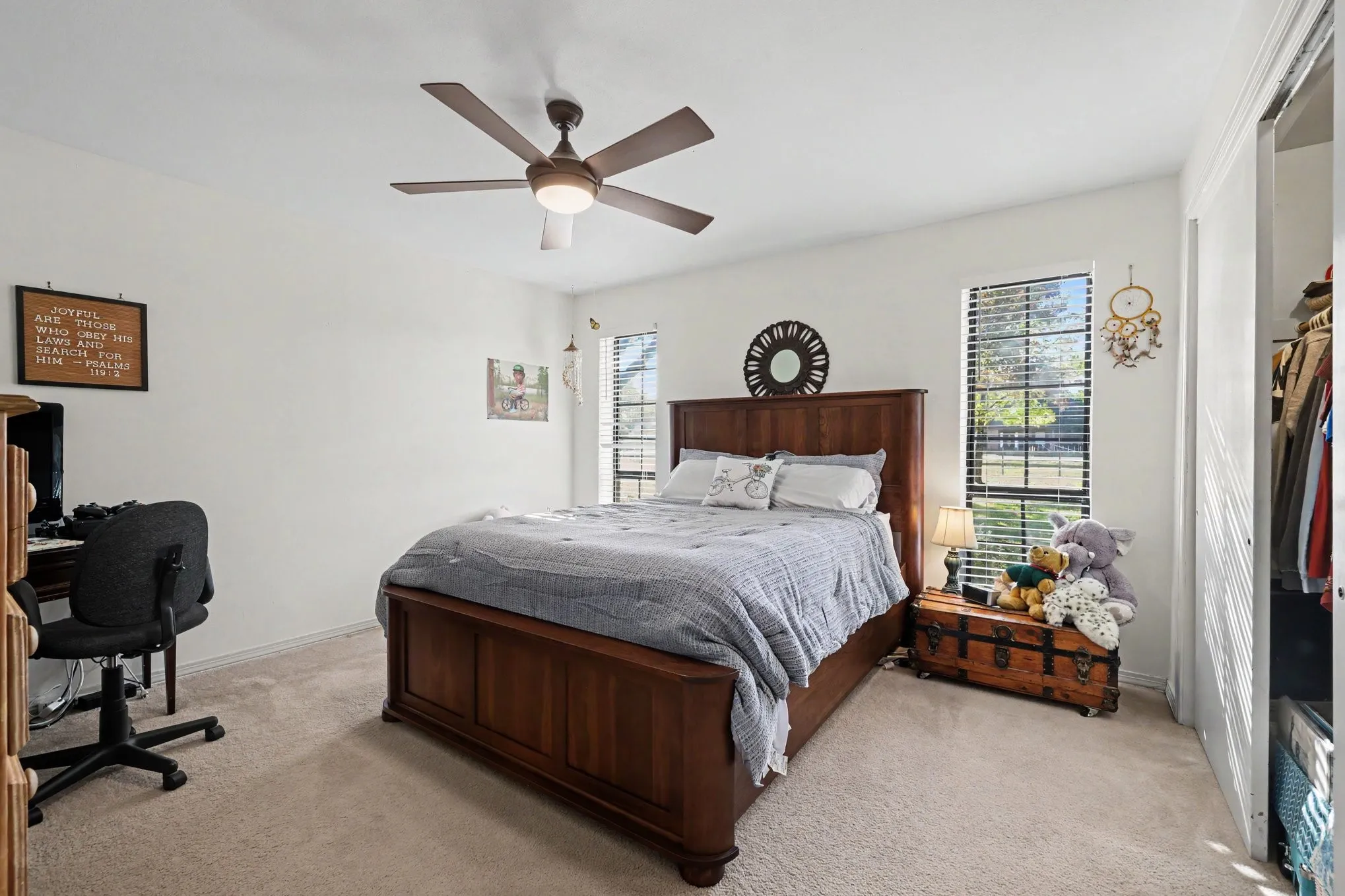Spacious primary bedroom featuring a wood-finish bed frame, ceiling fan with integrated lighting, neutral carpet flooring, and natural light from multiple windows