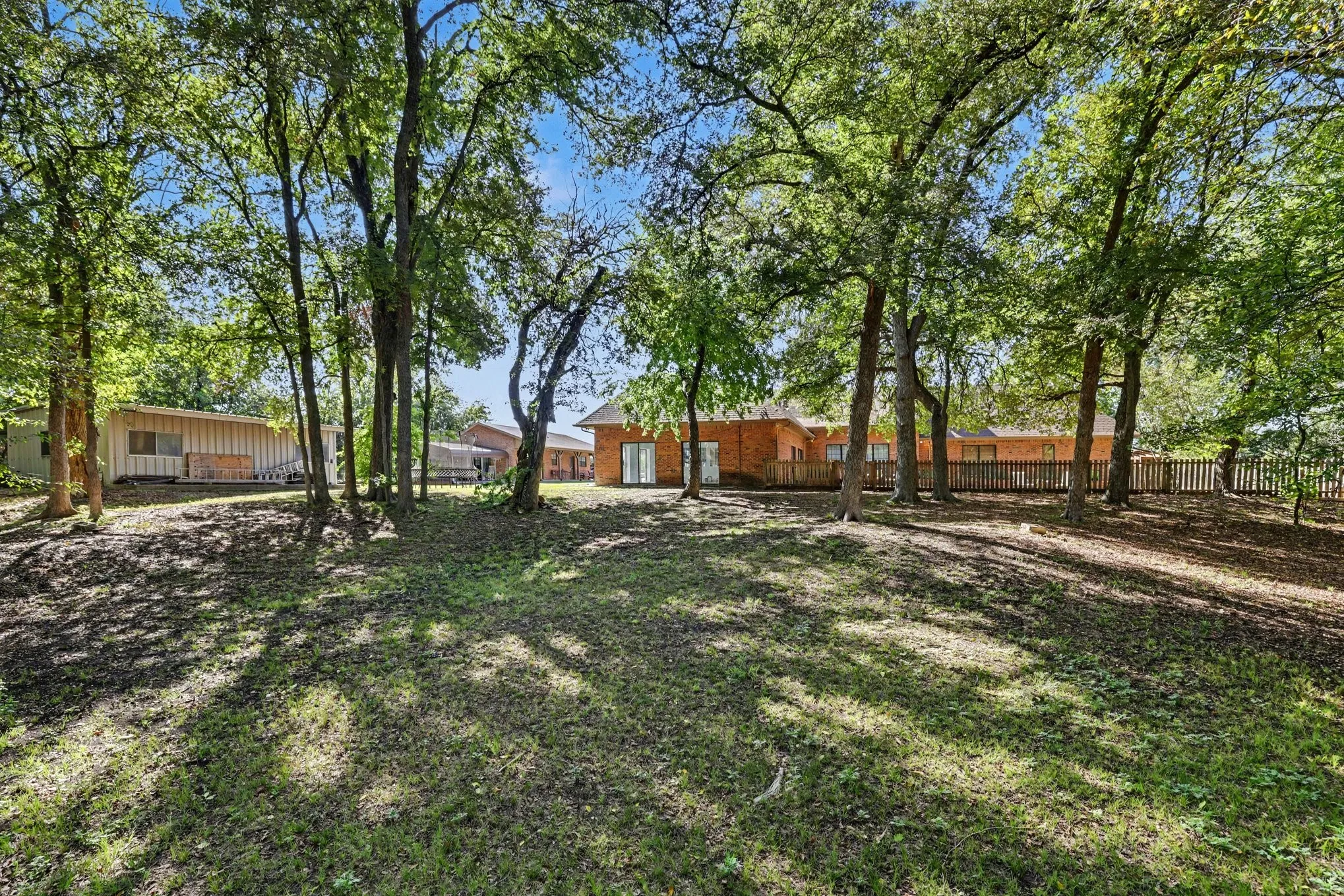 Expansive grassy yard with mature trees, a wood deck, and a wood fence