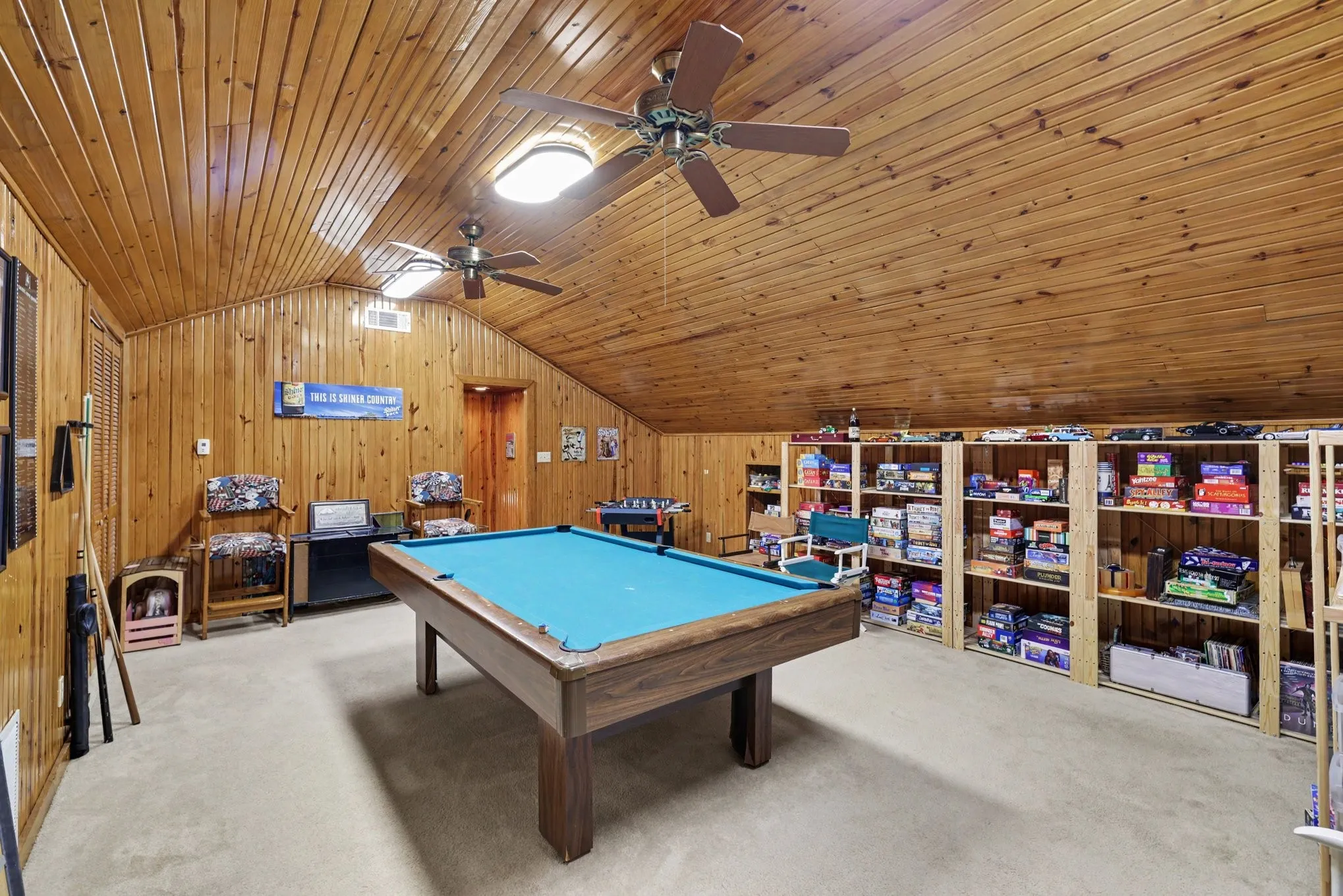 Wood-paneled walls and ceiling, two ceiling fans with integrated lighting, built-in shelving, and light-toned carpeting