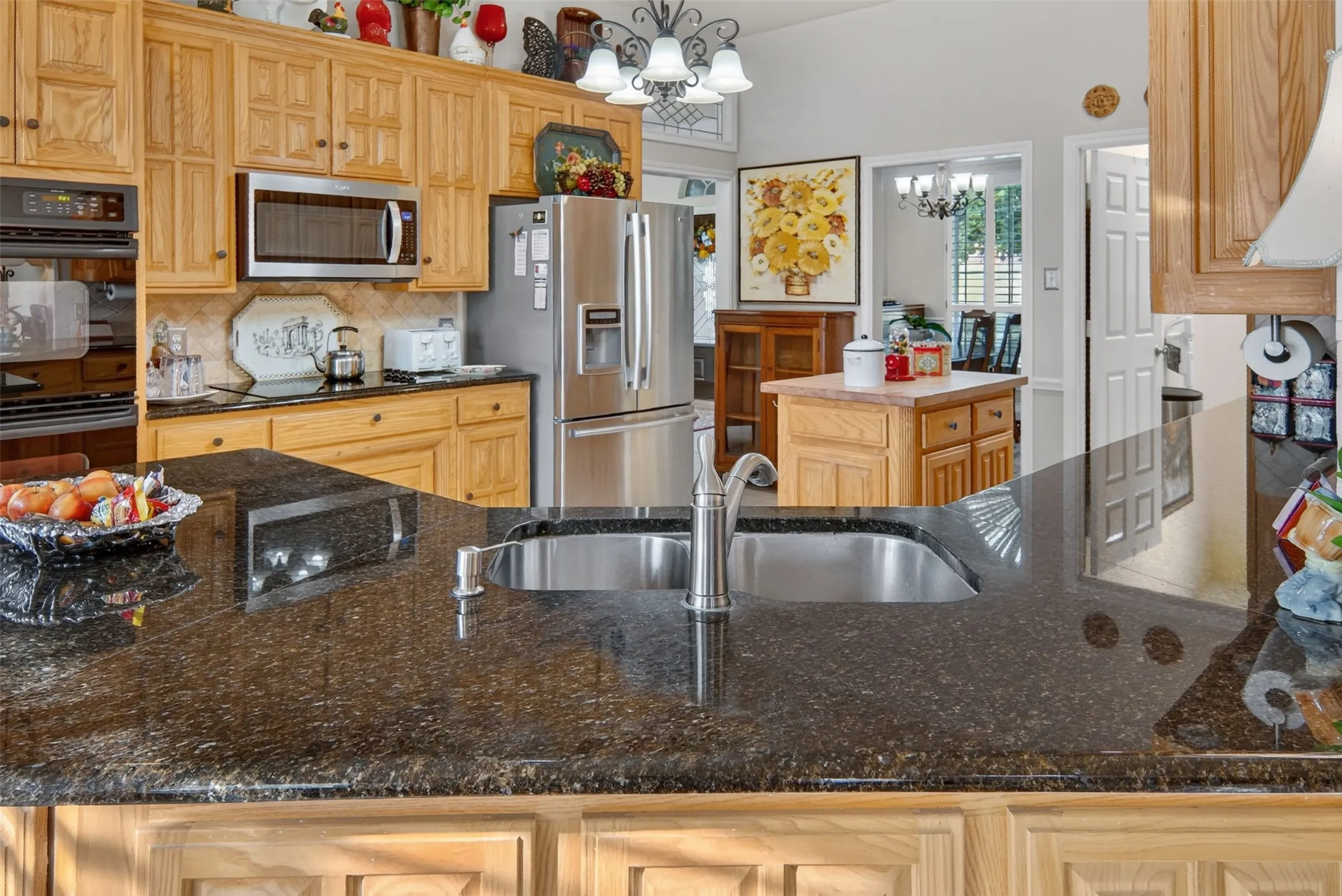 Kitchen featuring granite countertops, a stainless steel sink with a gooseneck faucet, light wood cabinetry, and stainless steel appliances