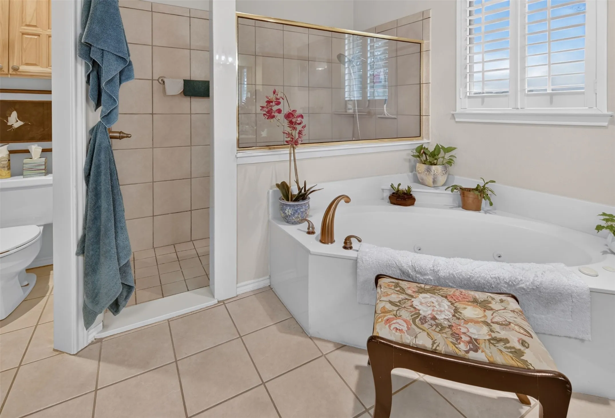 Built-in corner soaking tub with deck-mounted fixtures, separate shower with tile surround and glass enclosure, and white window shutters