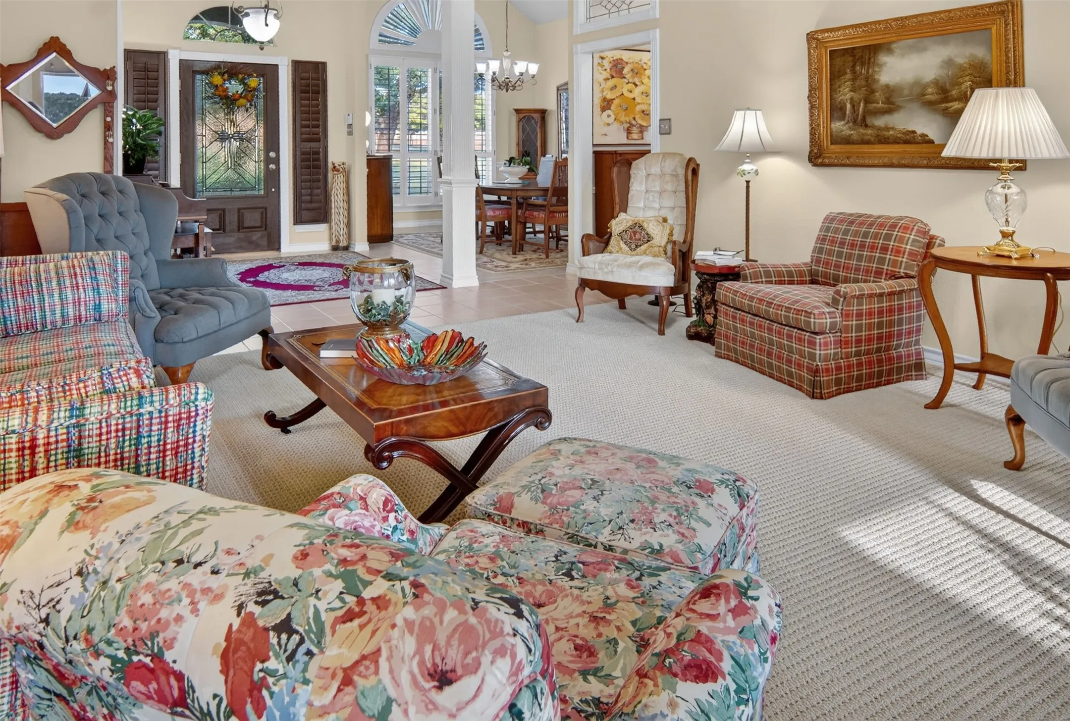 Elegant primary living space showcasing neutral wall finishes, natural light from multiple windows and glass doors, hardwood-finish flooring throughout, and a mix of upholstered seating with traditional wood-frame furnishings