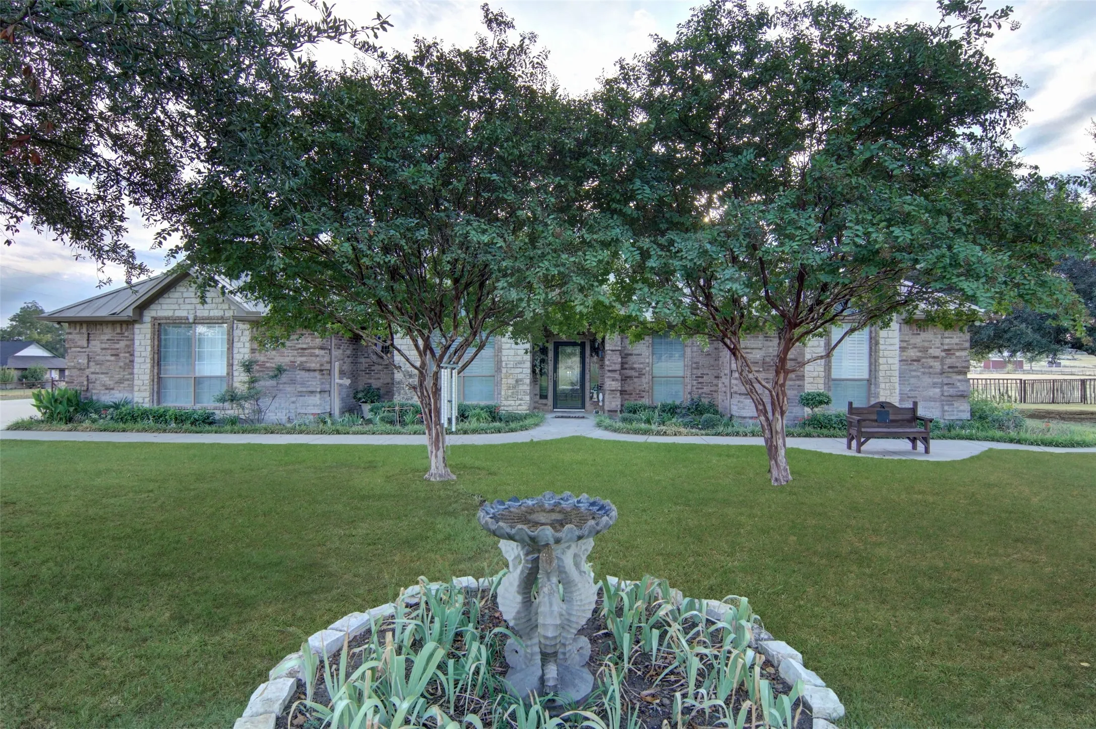 Stone exterior with a dark metal roof, mature trees, manicured lawn, and paved​​‌​​​​‌​​‌‌​‌‌​​​‌‌​‌​‌​‌​​​‌​​ walkways