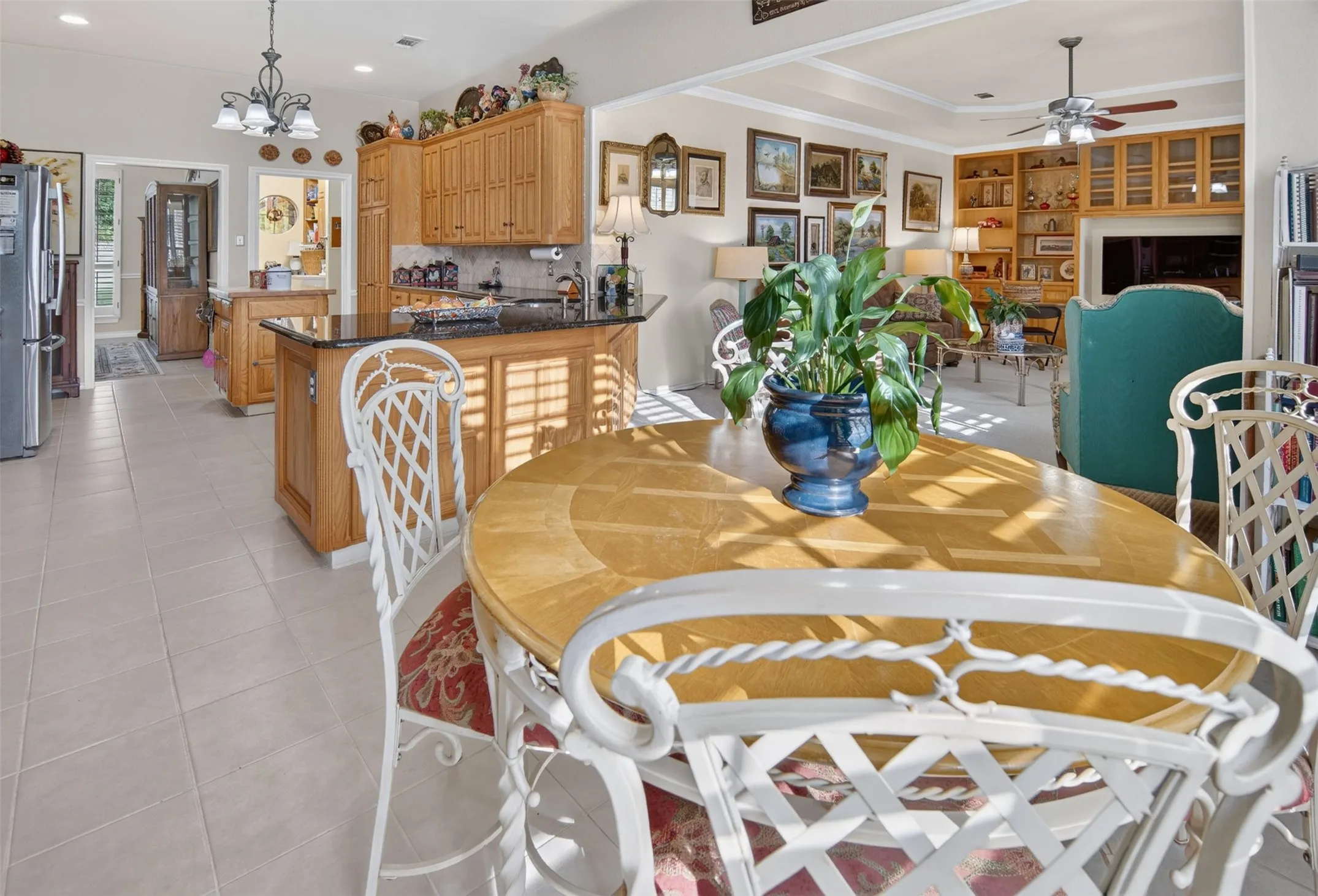Open-concept living and dining area featuring tile flooring, wood cabinetry throughout, stainless steel appliances, granite countertops, and abundant natural light from multiple windows and skylights