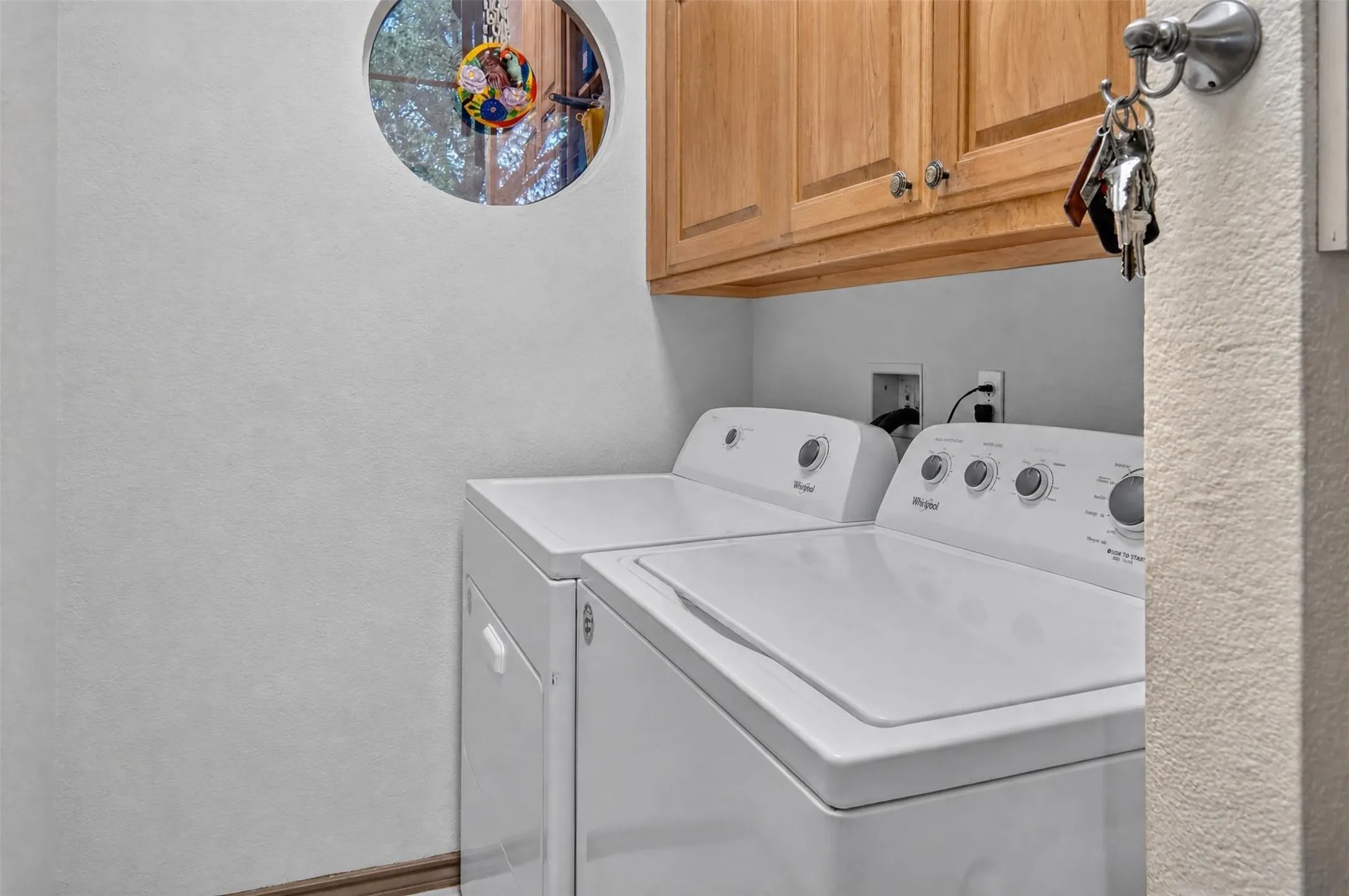 Wood-finish cabinetry with silver-tone hardware, white appliances, and a circular window