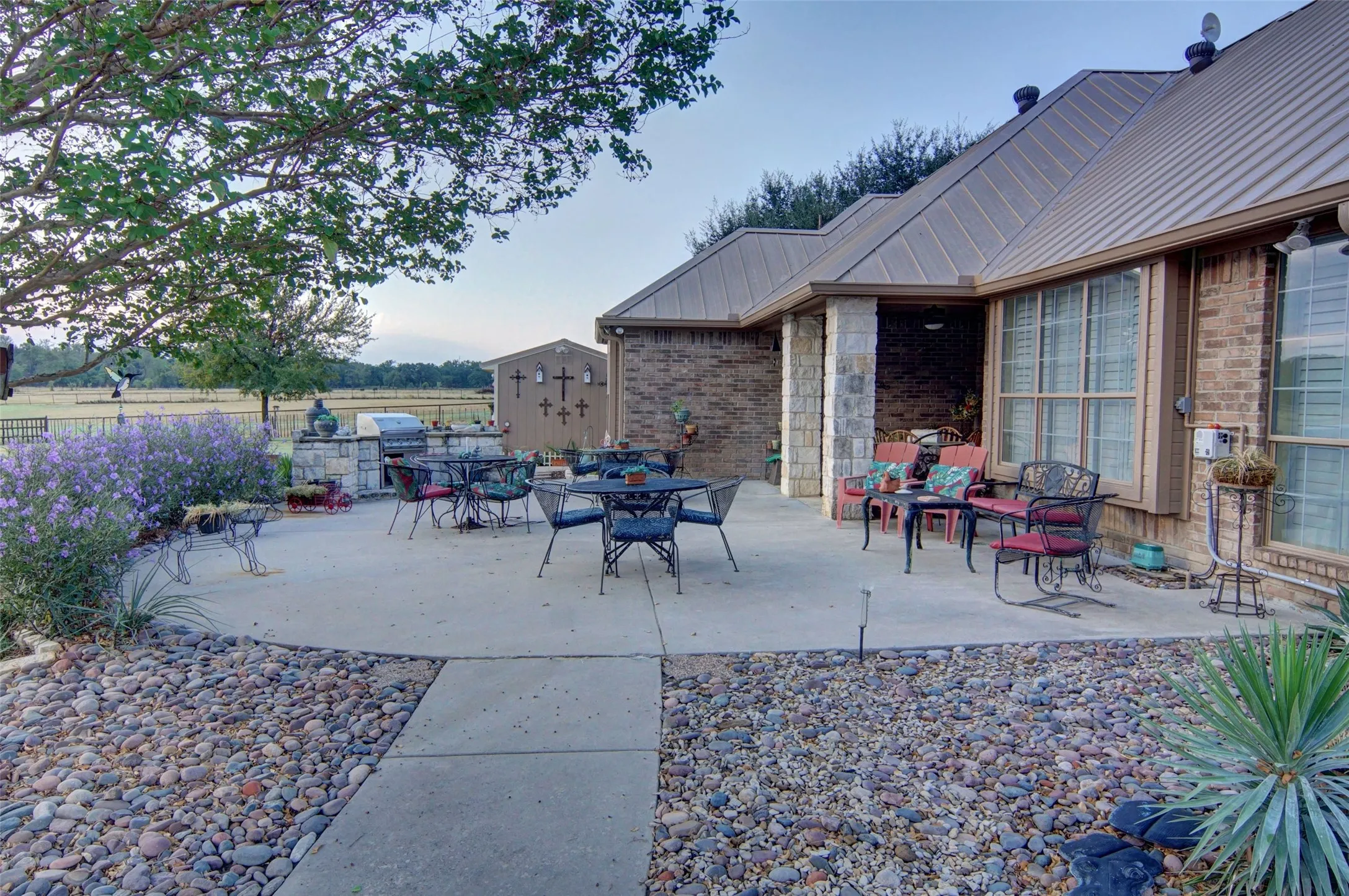 Expansive concrete patio with an integrated outdoor kitchen, brick and stone exterior, and a durable metal roof