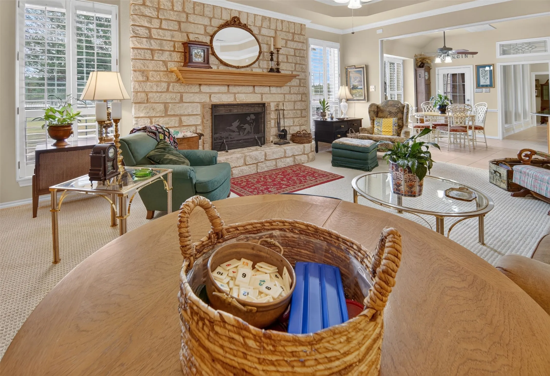 Stone-clad fireplace with a wood mantle, neutral-toned carpeting, and plantation shutters on multiple windows