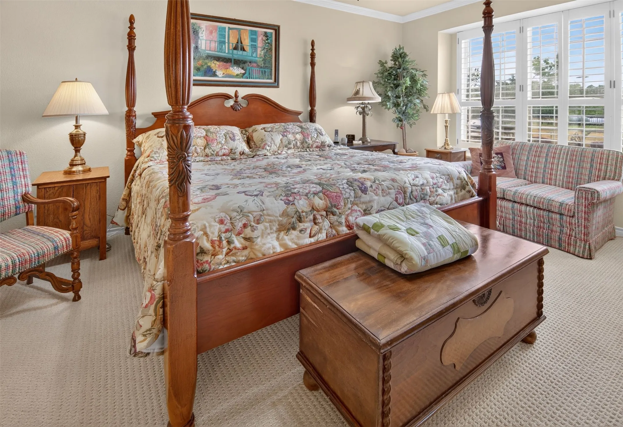 Carpeted flooring, window with plantation shutters, crown molding, and two side tables with lamps