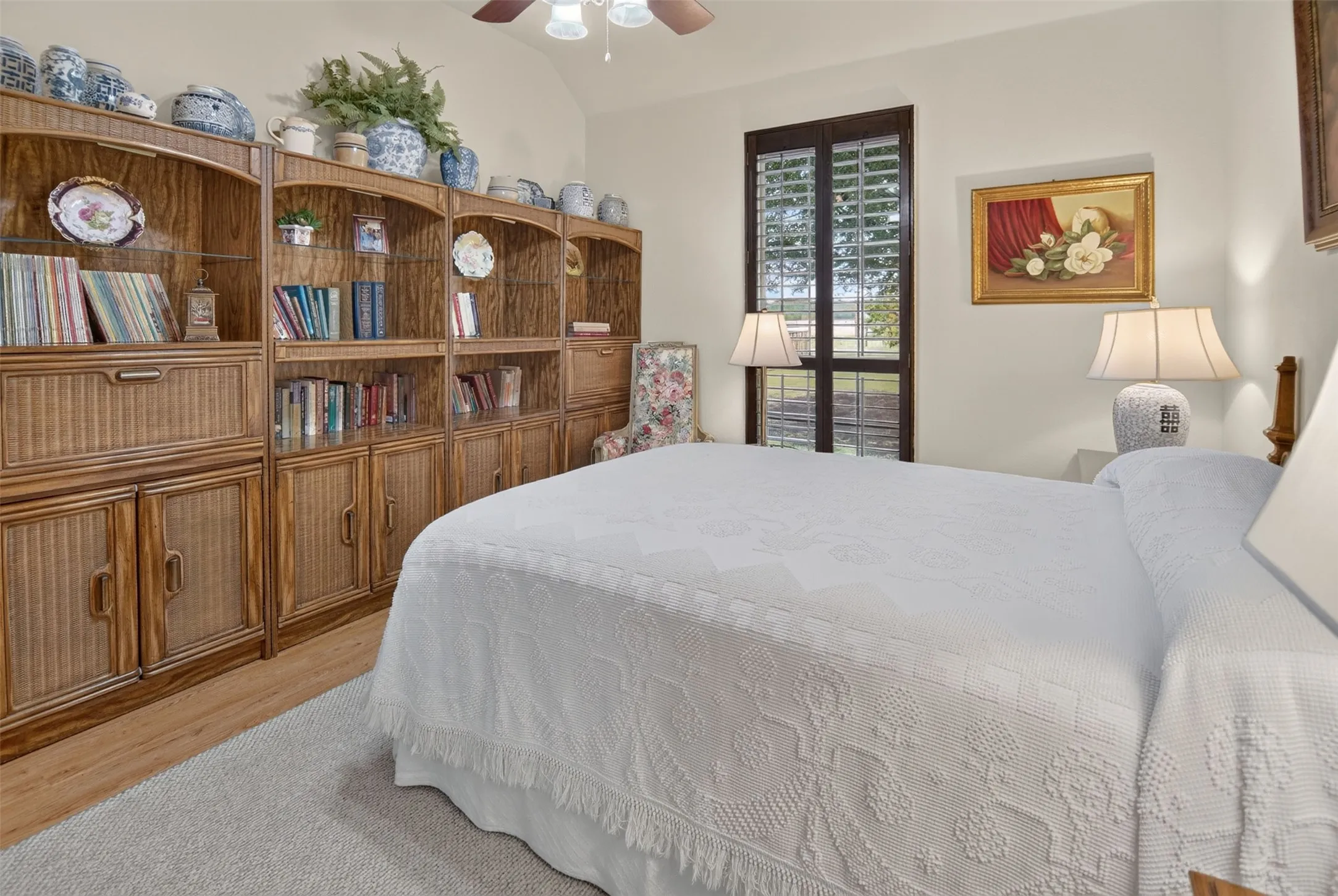 Built-in shelving with integrated cabinetry, wood-finish flooring, ceiling fan, and window with plantation shutters