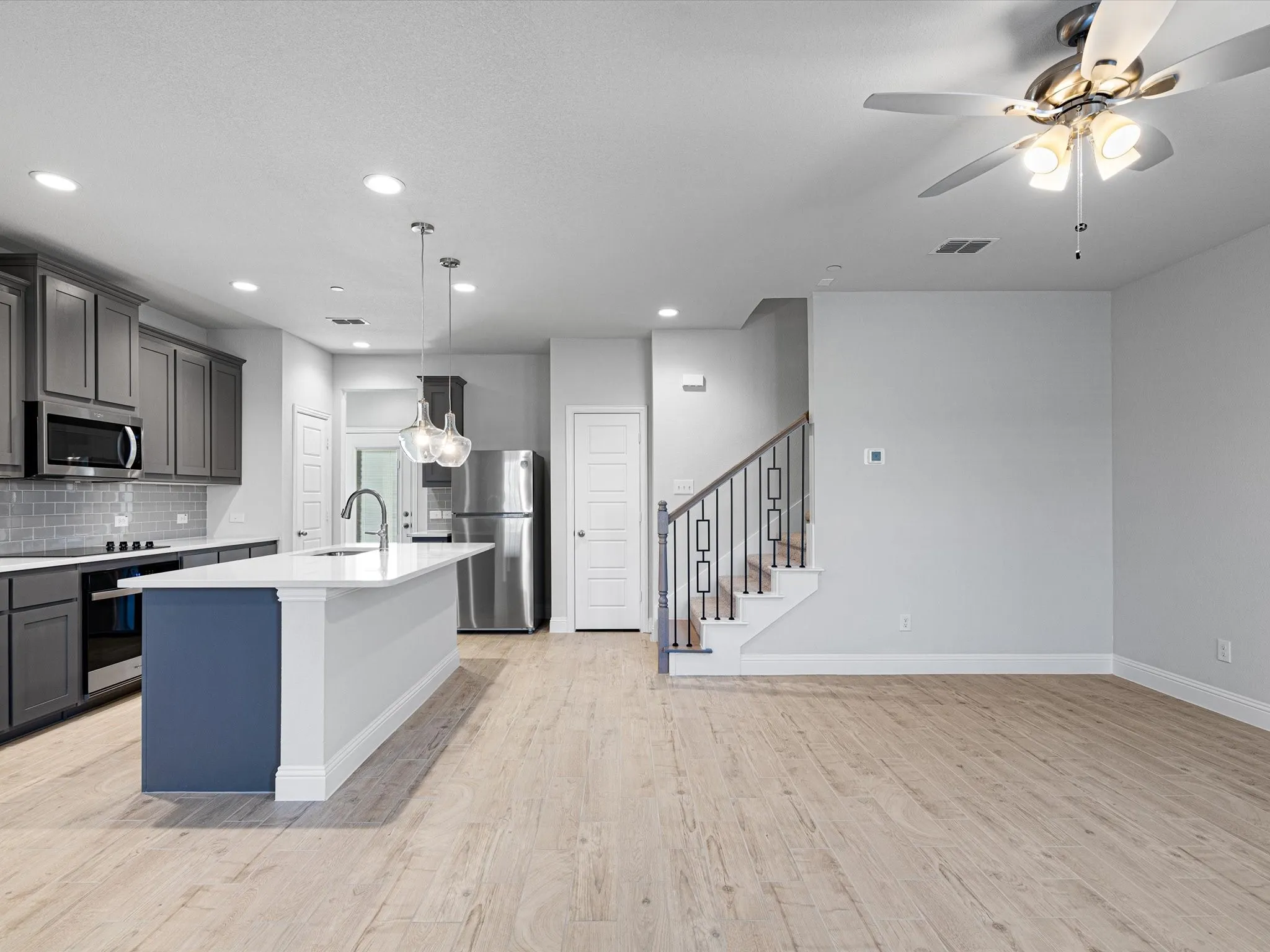 Open-concept living area with wood-finish flooring, a contemporary kitchen, and a staircase featuring metal balusters