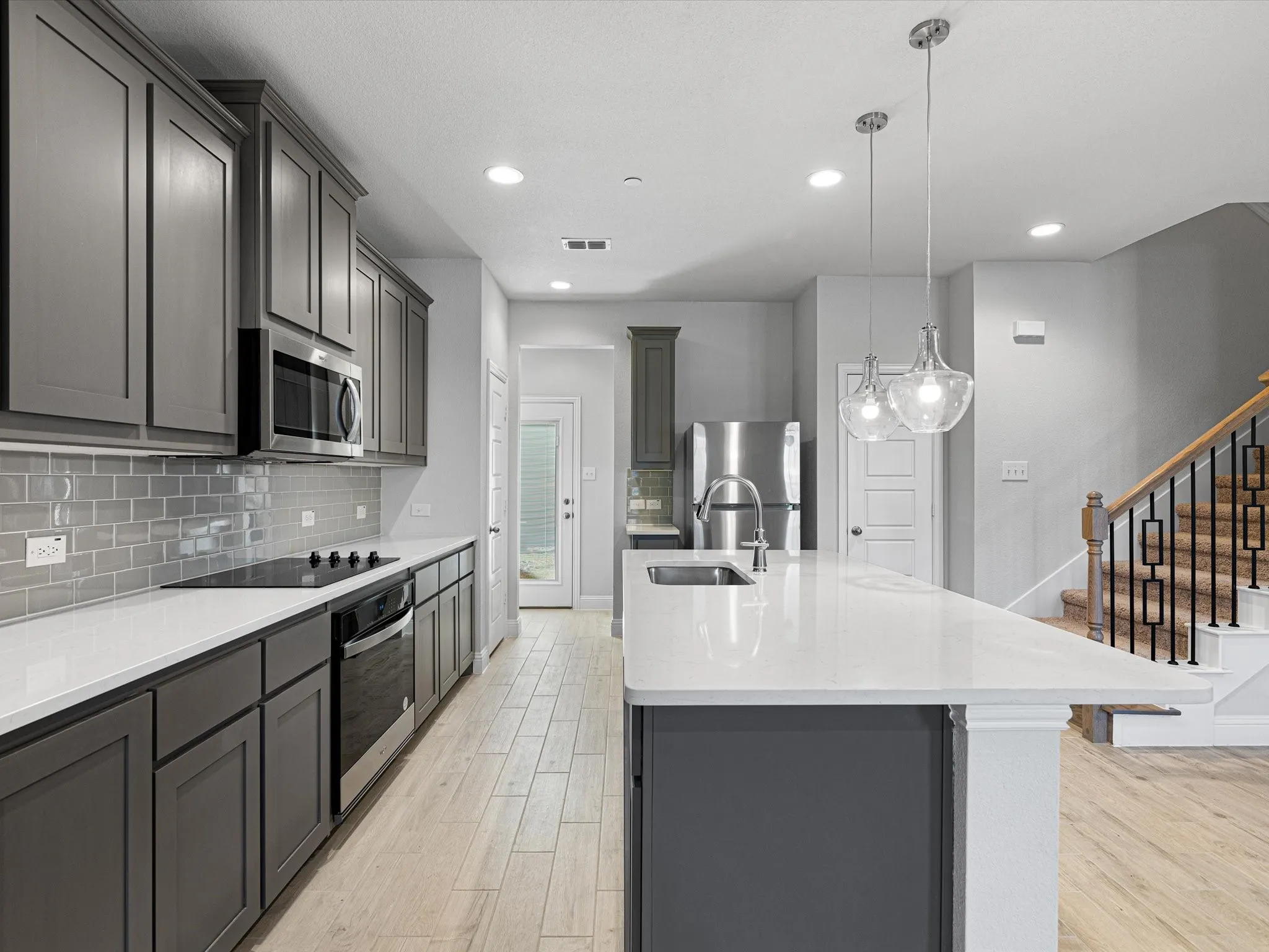 Contemporary kitchen featuring dark gray cabinetry, white countertops, subway tile backsplash, and stainless steel appliances