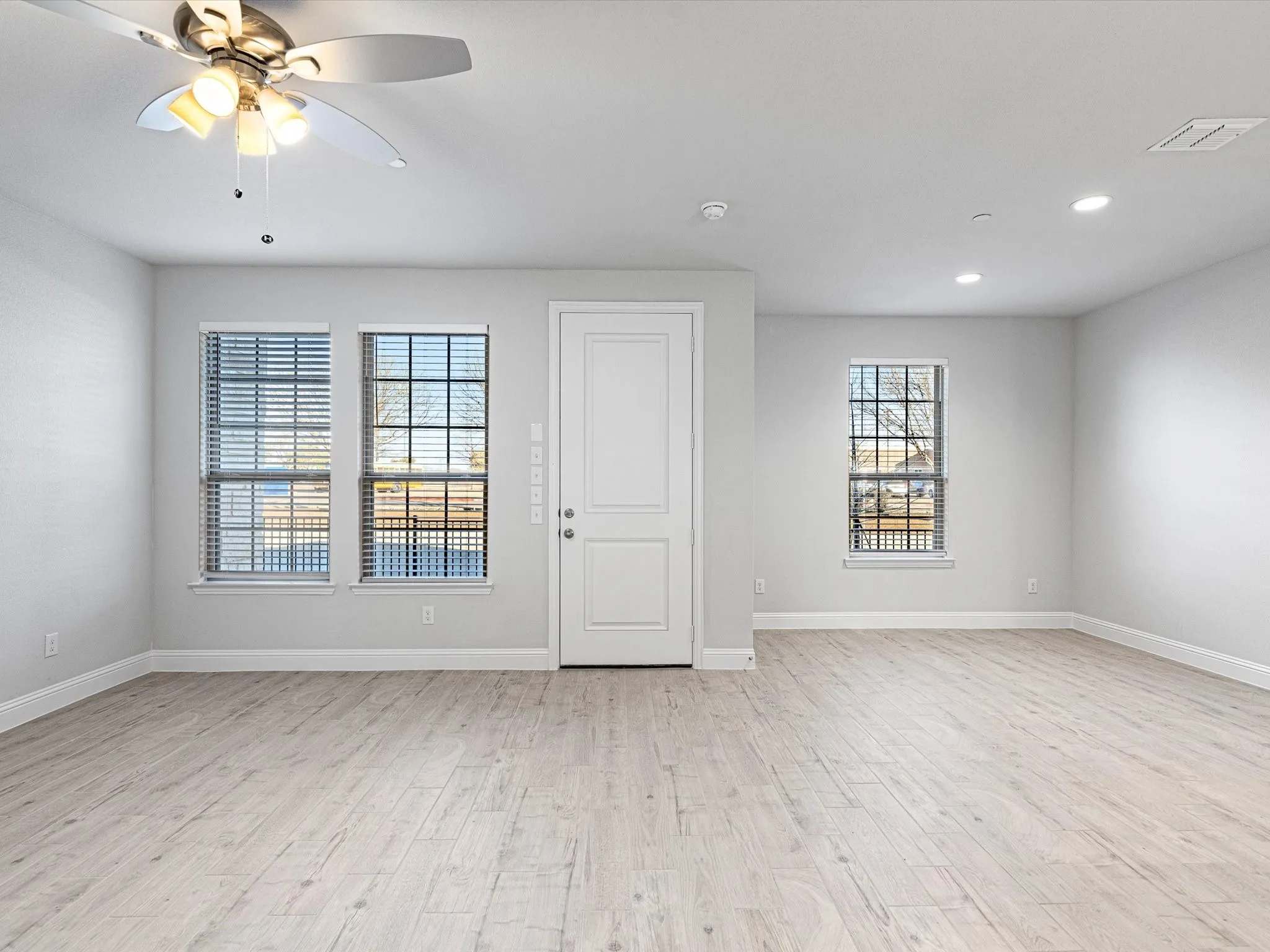Recessed lighting, ceiling fan with light fixture, wood-finish flooring, multiple windows, and a panel door