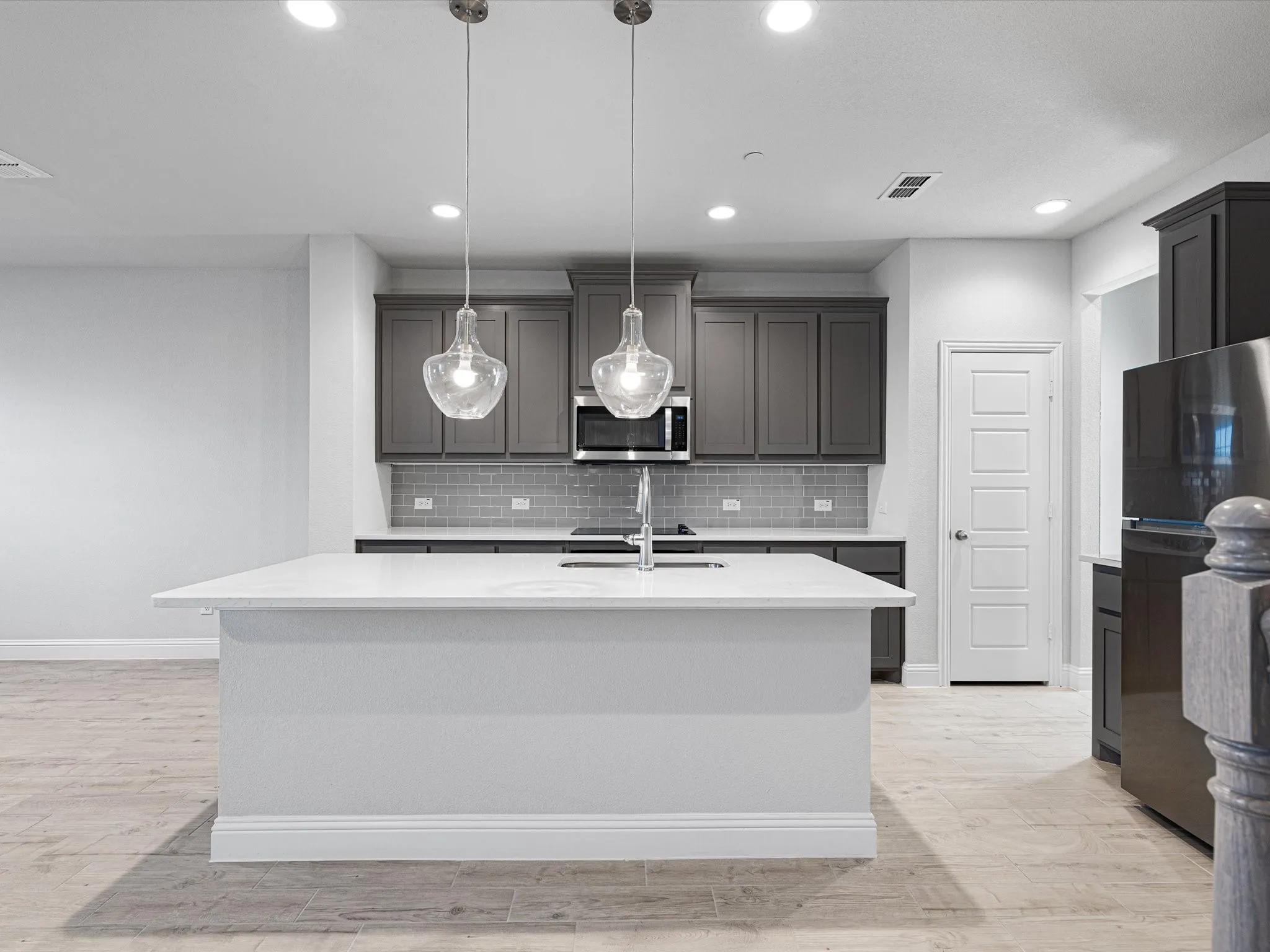 Kitchen featuring a center island with a light-toned countertop, dark shaker-style cabinetry, stainless steel appliances, a gray subway tile backsplash, and recessed lighting