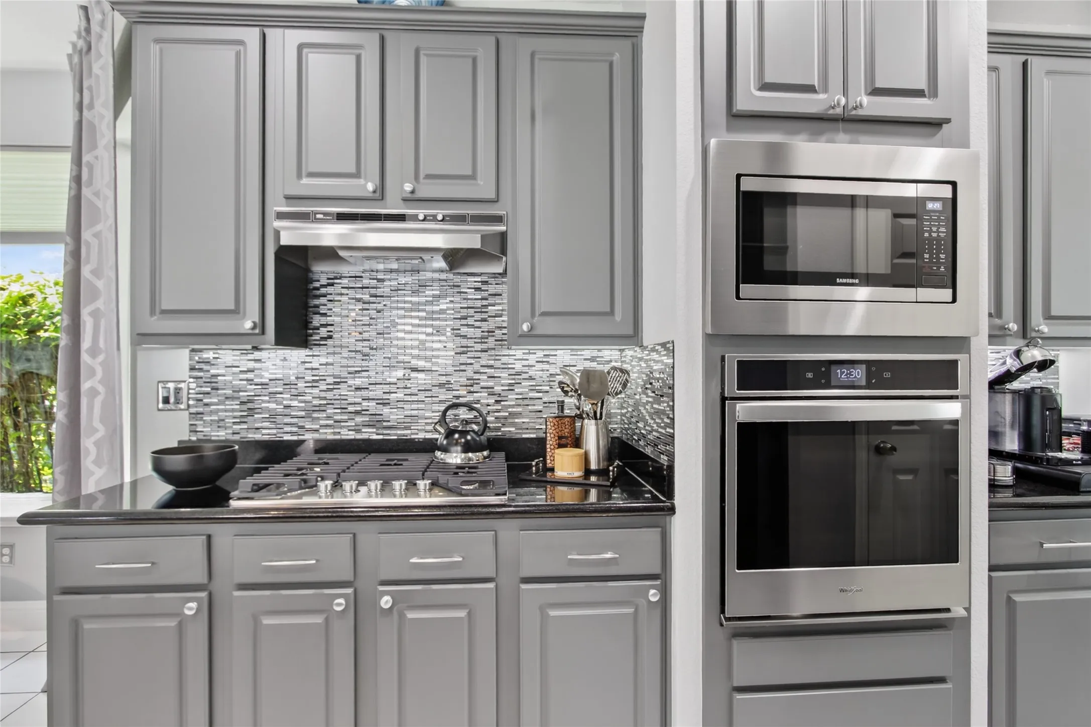 View of gas range with outside vented hood. Sleek, modern glass backsplash is easy to clean. Built in microwave and oven. New Oven 2019.  New Whirlpool cooktop added in 2025
