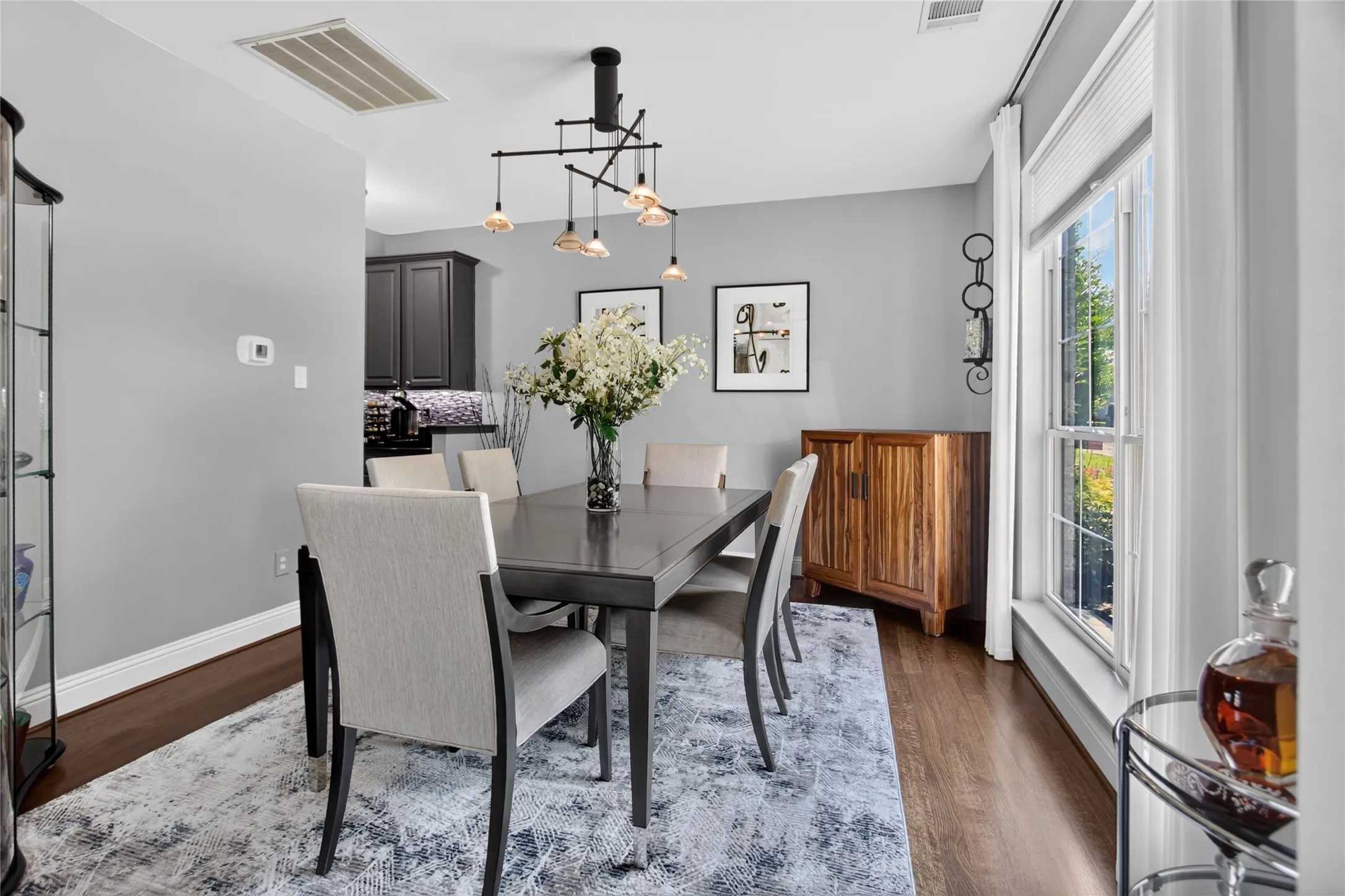 View of dining area to the right as you enter the home. Statement light fixture. Wood floors, light soft grey walls. Window looks out onto the front landscaping. Entrance at the rear is pass through to the Kitchen.